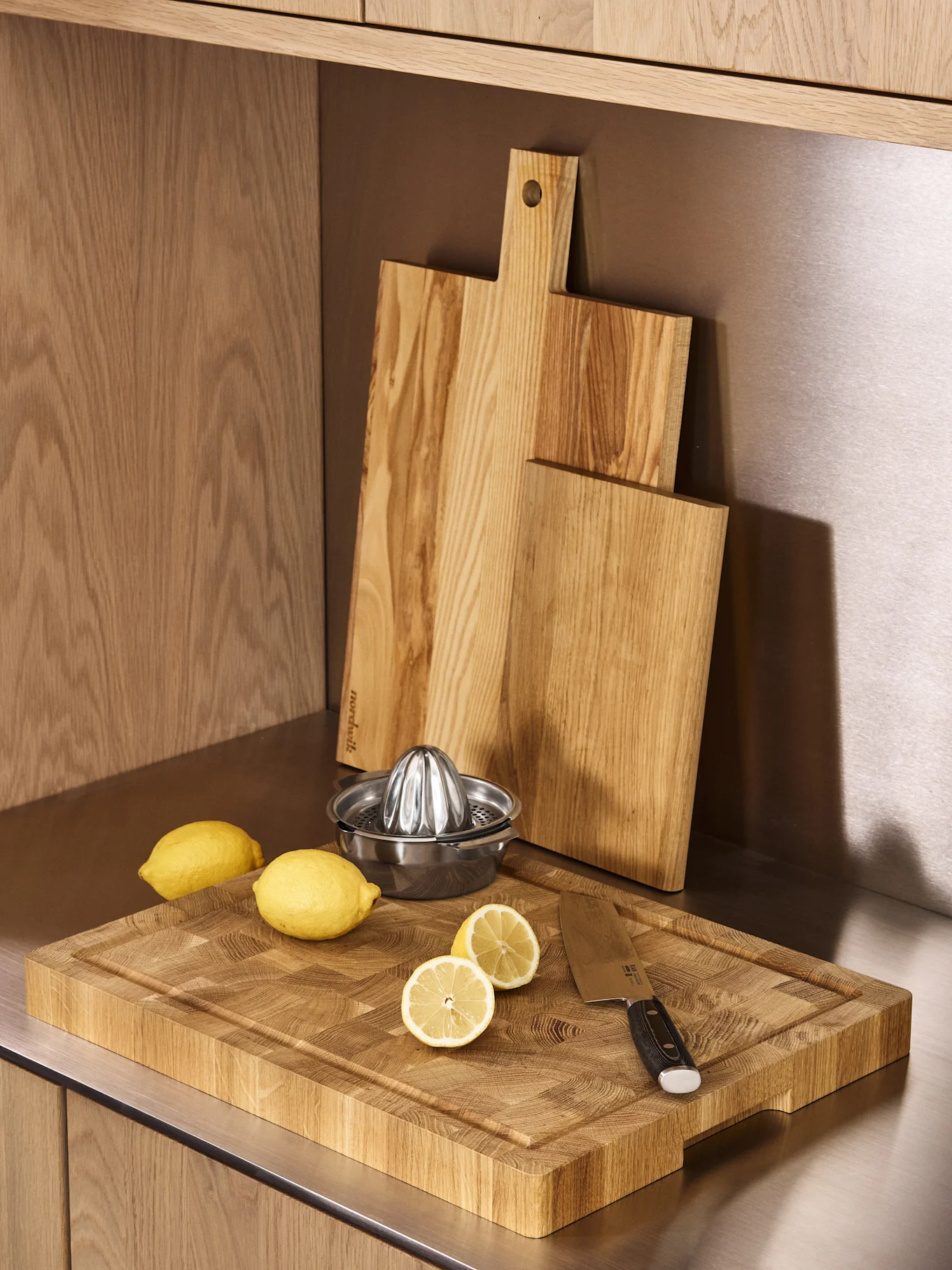 Three wooden cutting boards, a stainless steel lemon squeezer, and fresh lemons on a kitchen counter.