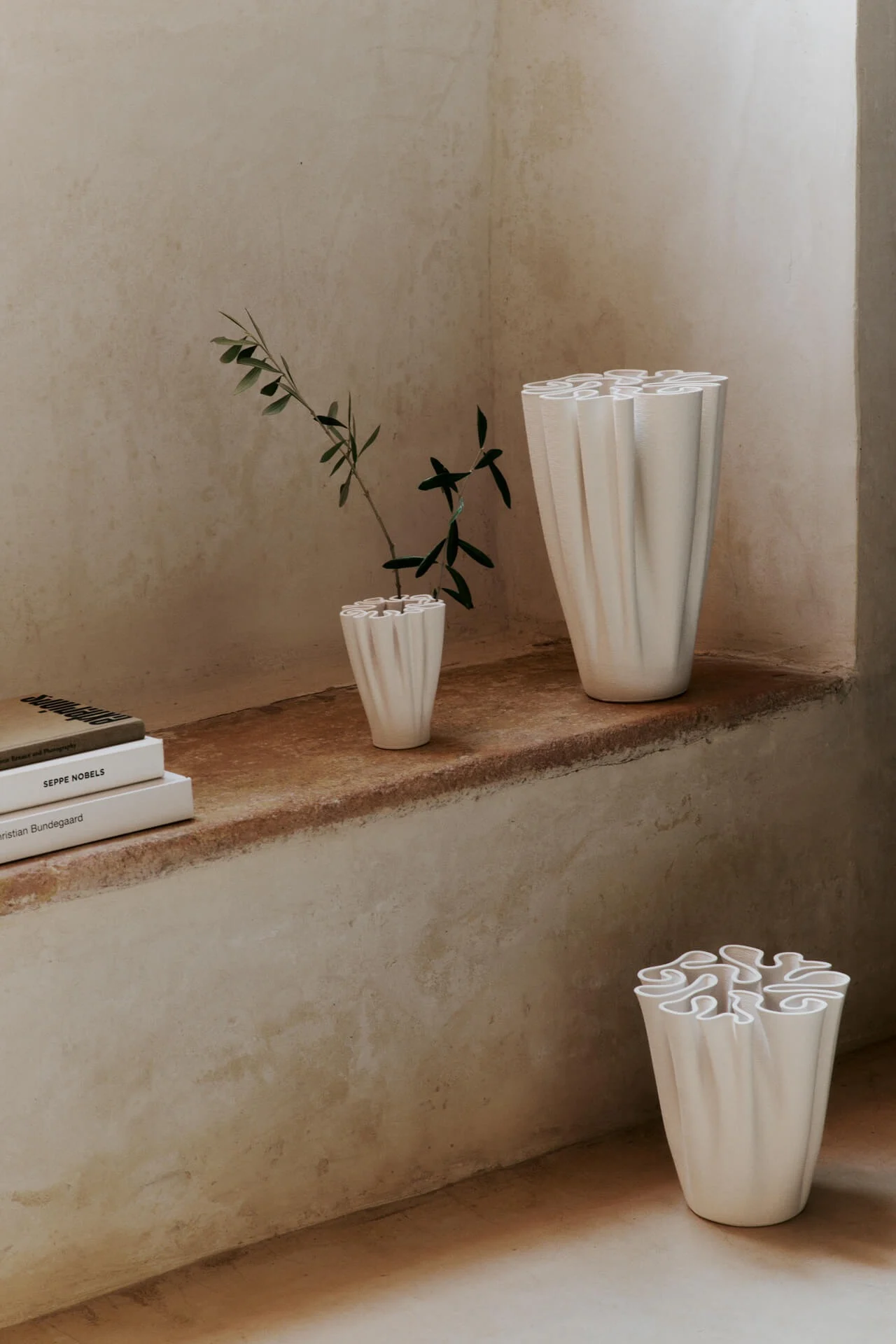 Three white, ruffled vases displayed in a rustic room, one with a green plant.
