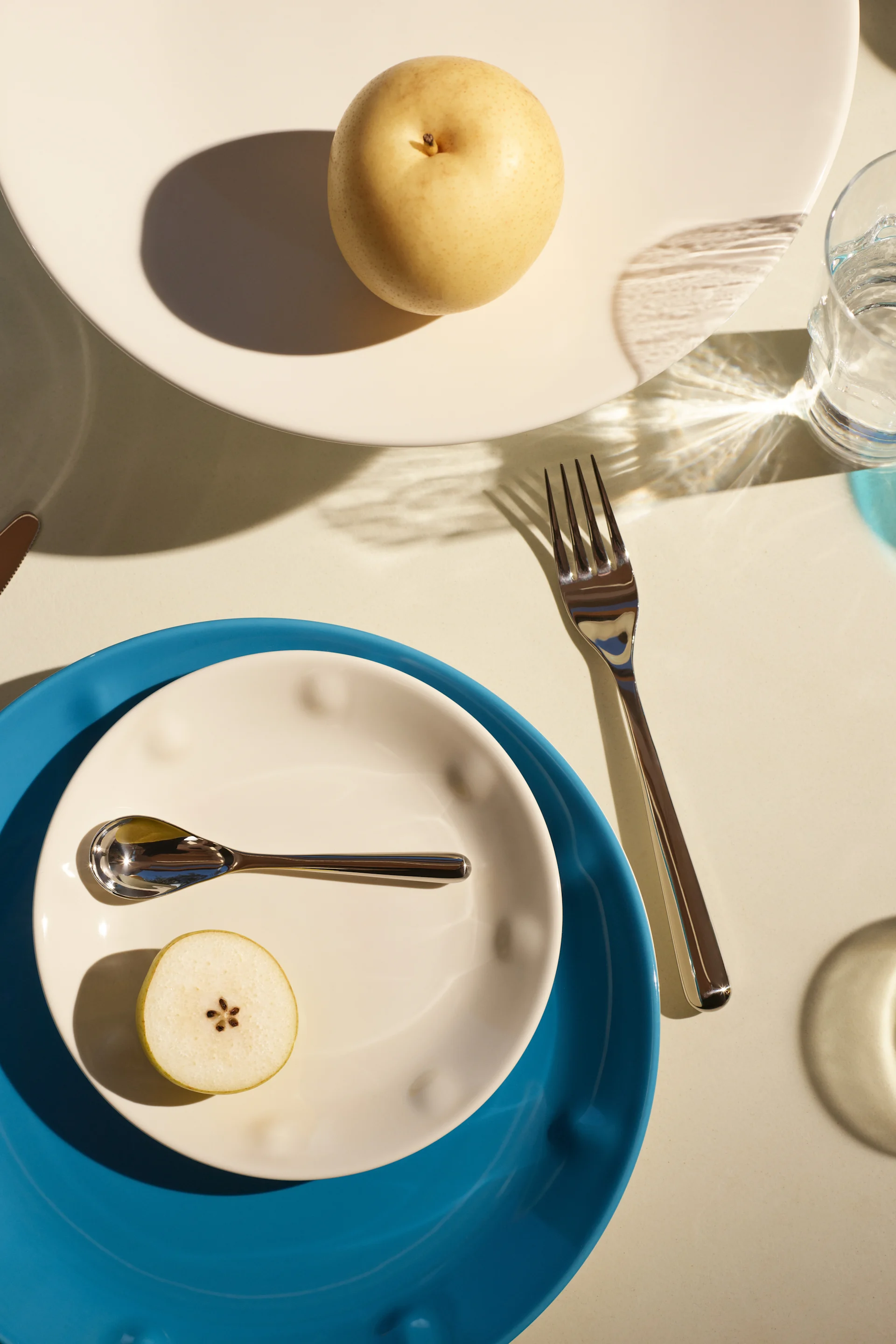 A white bowl placed on top of a blue plate with a glass and cutlery from the Solare Collection from Iittala. 