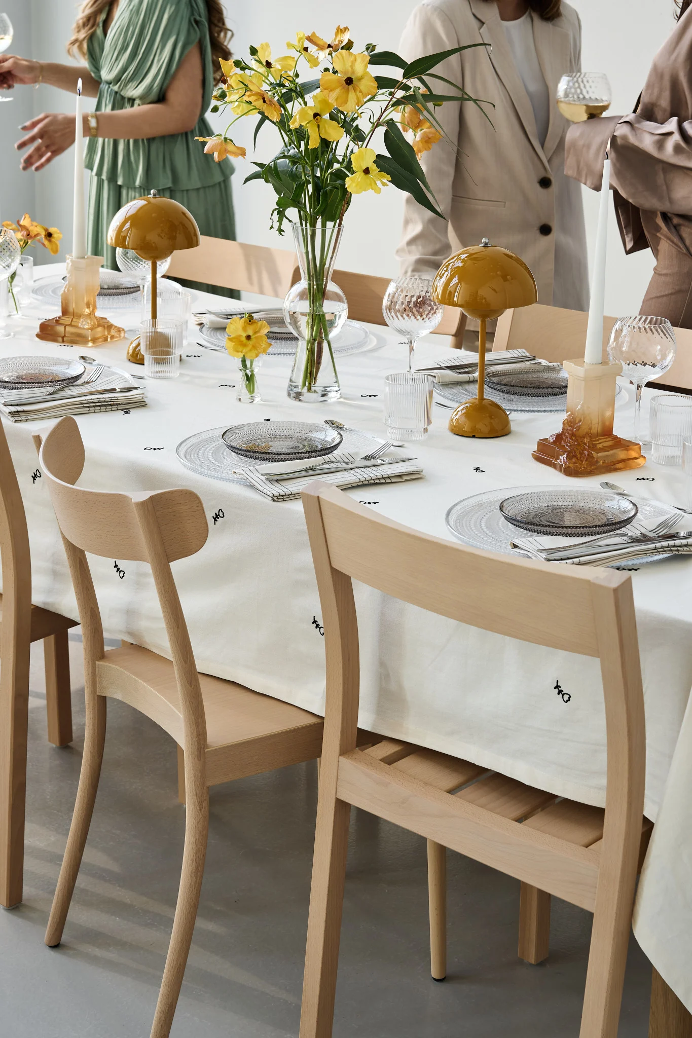 A party table setting with yellow accents and guests mingling around. Here you see the Flowerpot VP9 from Tradition with the Rocky Baroque candle holder in amber.  