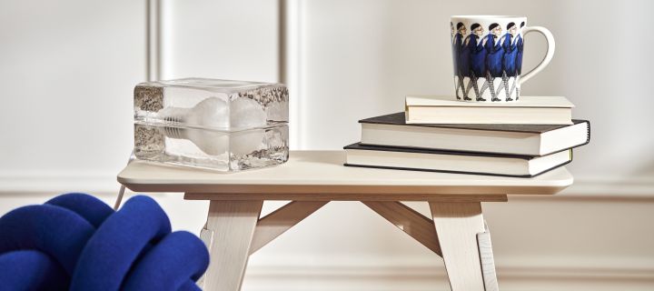 A small table in white oak from Design House Stockholm, on it rests the lamp Block and Elsa Beskow mugs Uncle Blue on stacks of books in a stylish living room.