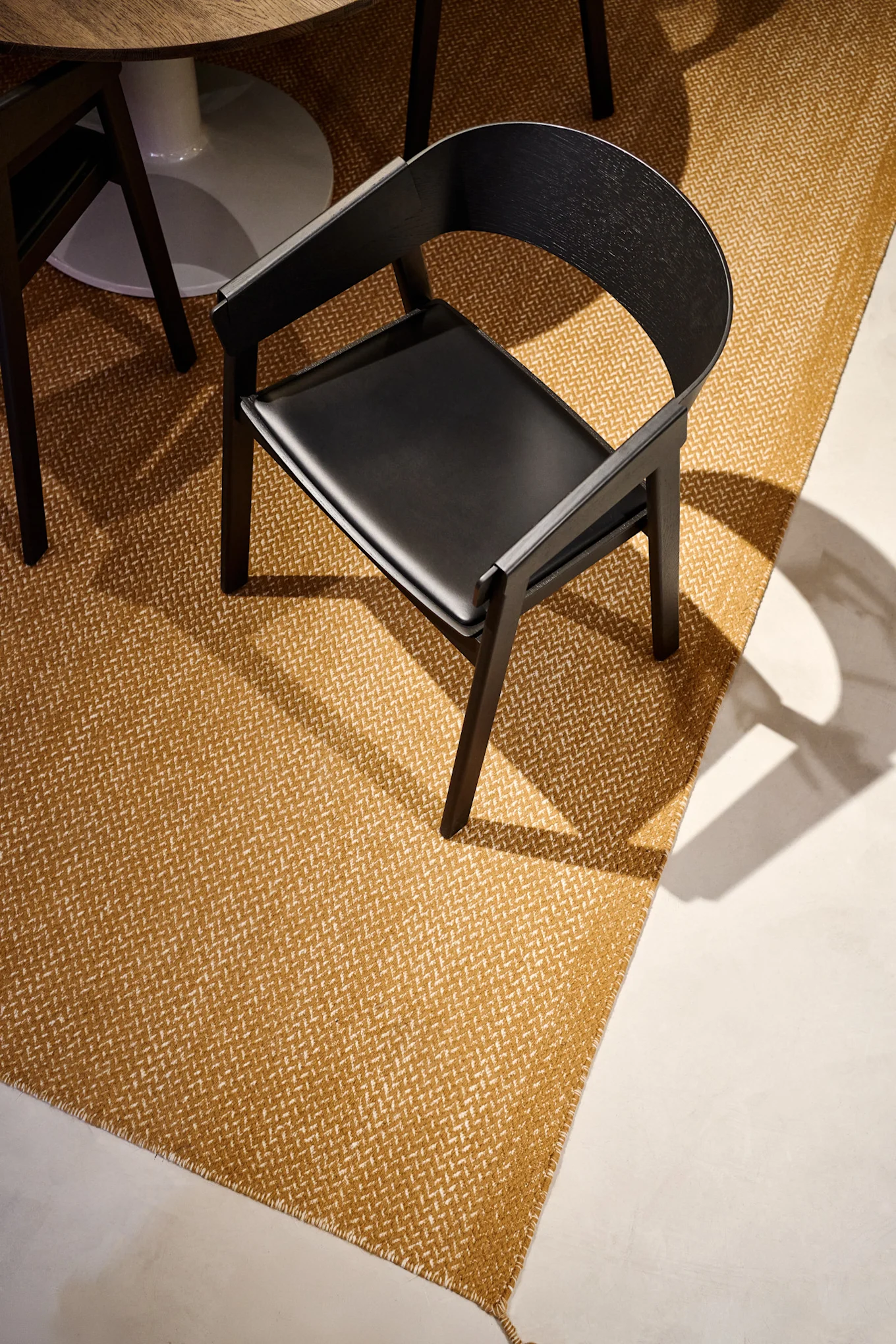 The black Cover armchair with leather seat from Muuto stands on a mustard-coloured rug.
