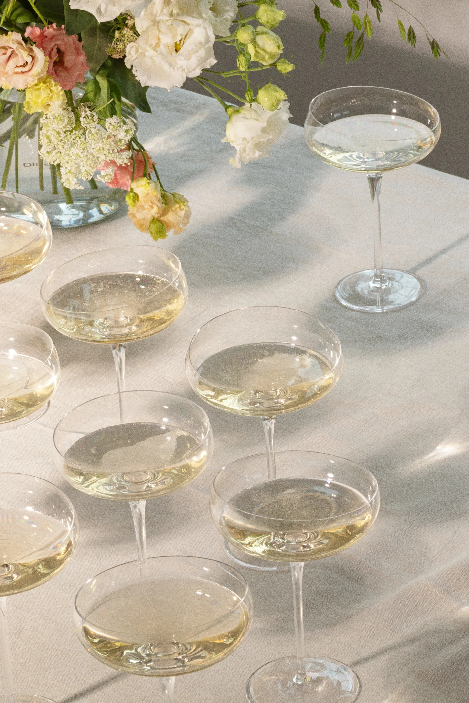 Champagne coupes with sparkling drinks on a table with a floral arrangement.