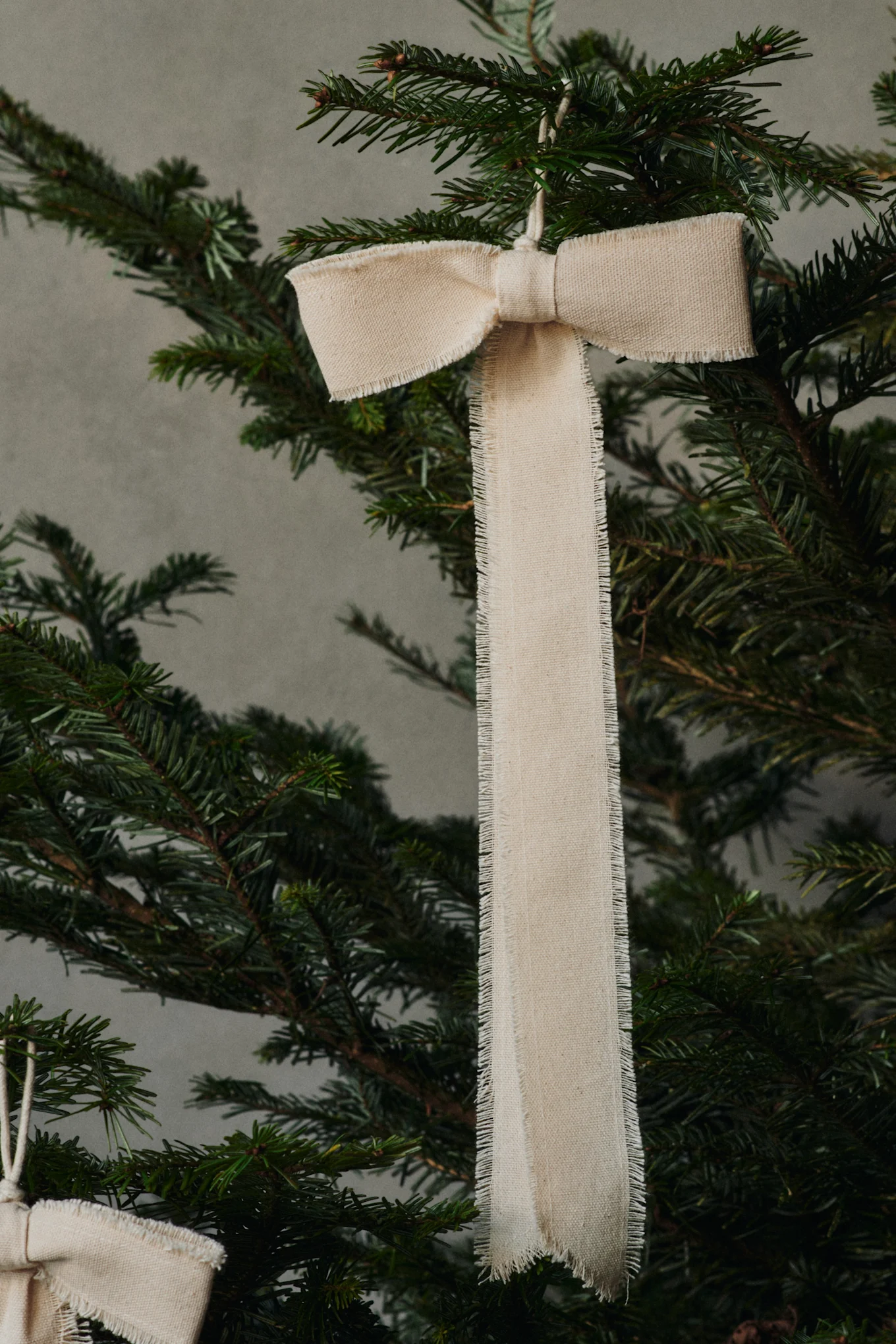 A bow-shaped decorative pendant by Ferm Living hangs from a Christmas tree.