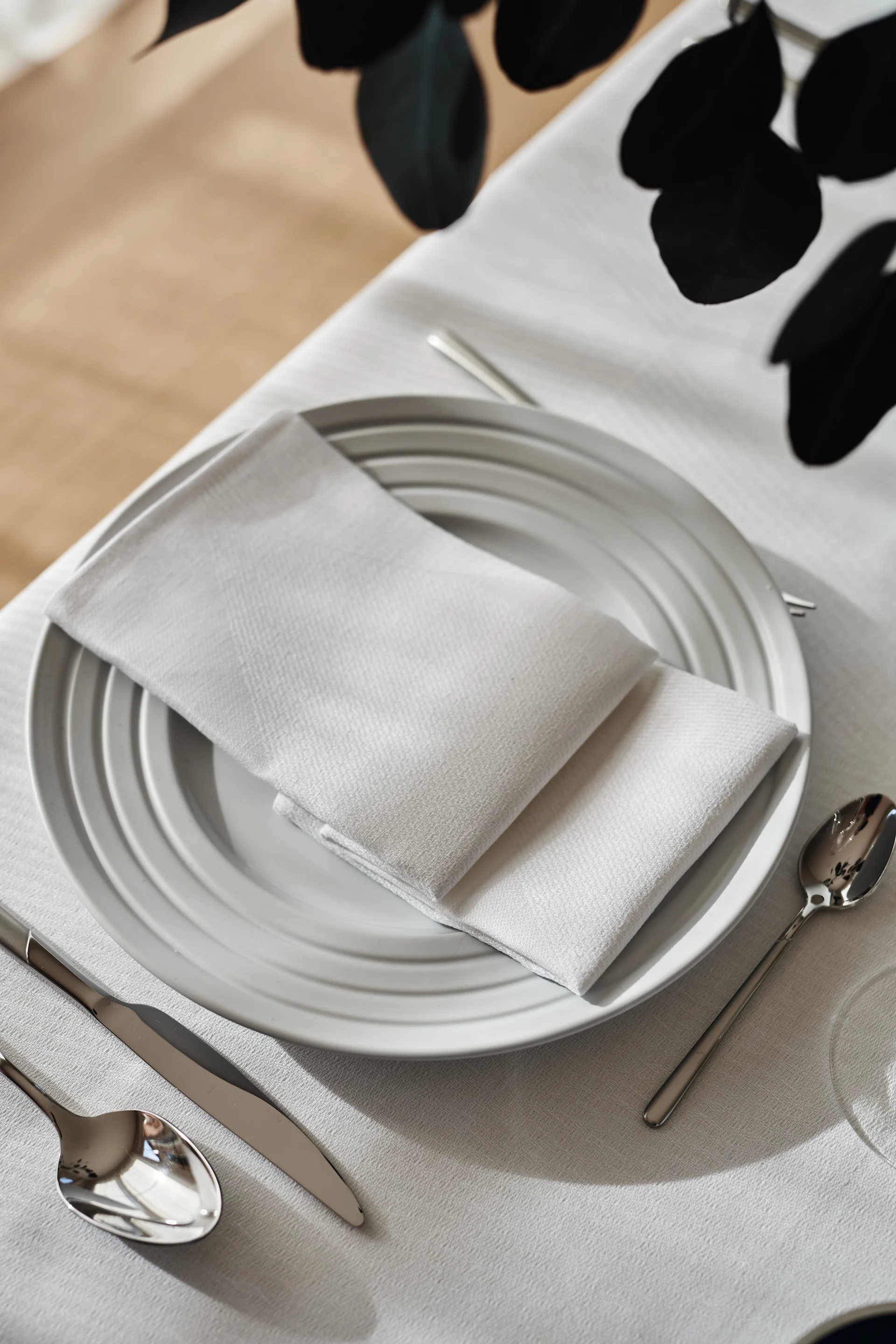 A crisp white table setting with a folded white napkin and white tablecloth and white porcelain from NJRD.