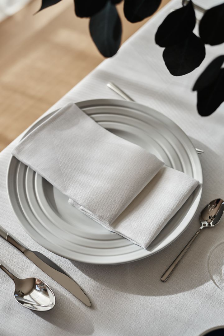 A crisp white table setting with a folded white napkin and white tablecloth and white porcelain from NJRD.