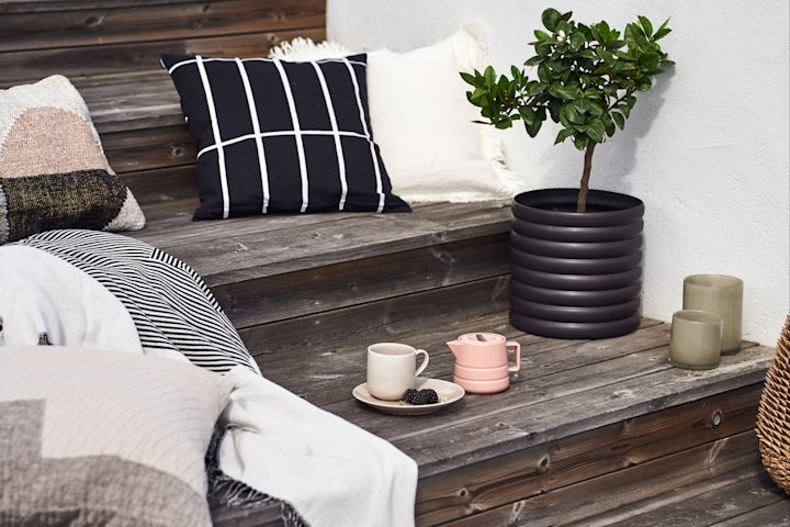 A set of stairs outside, decorated with lots of summer essentials such as plant pots, blankets and pillow and a tea cup and saucer. 