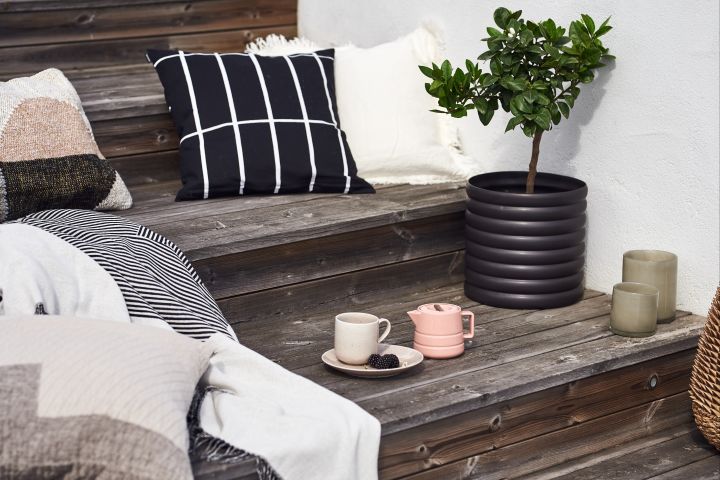 A set of stairs outside, decorated with lots of summer essentials such as plant pots, blankets and pillow and a tea cup and saucer. 