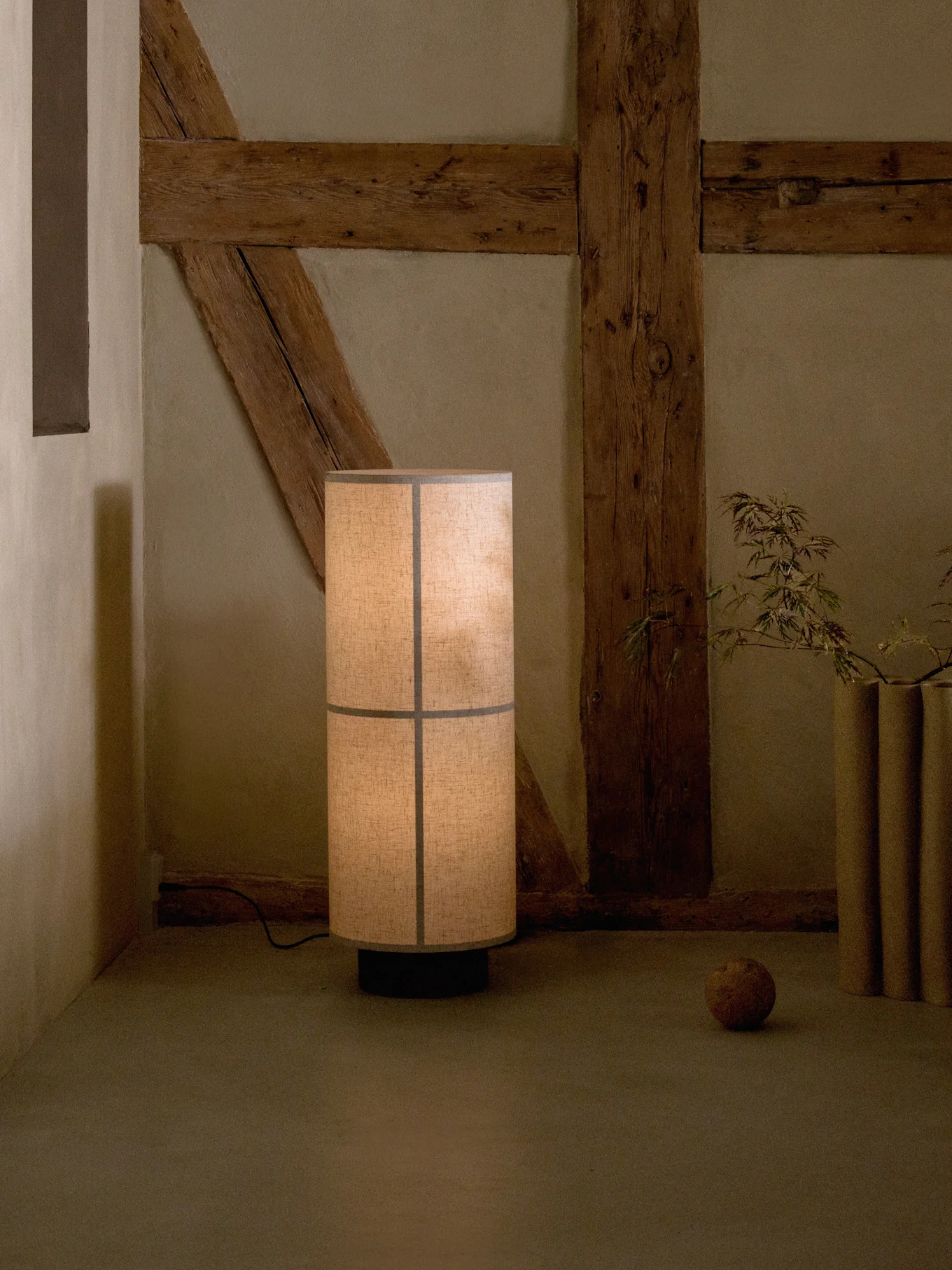 Tall floor lamp with a segmented fabric shade, casting a warm glow in a rustic room with exposed wooden beams.