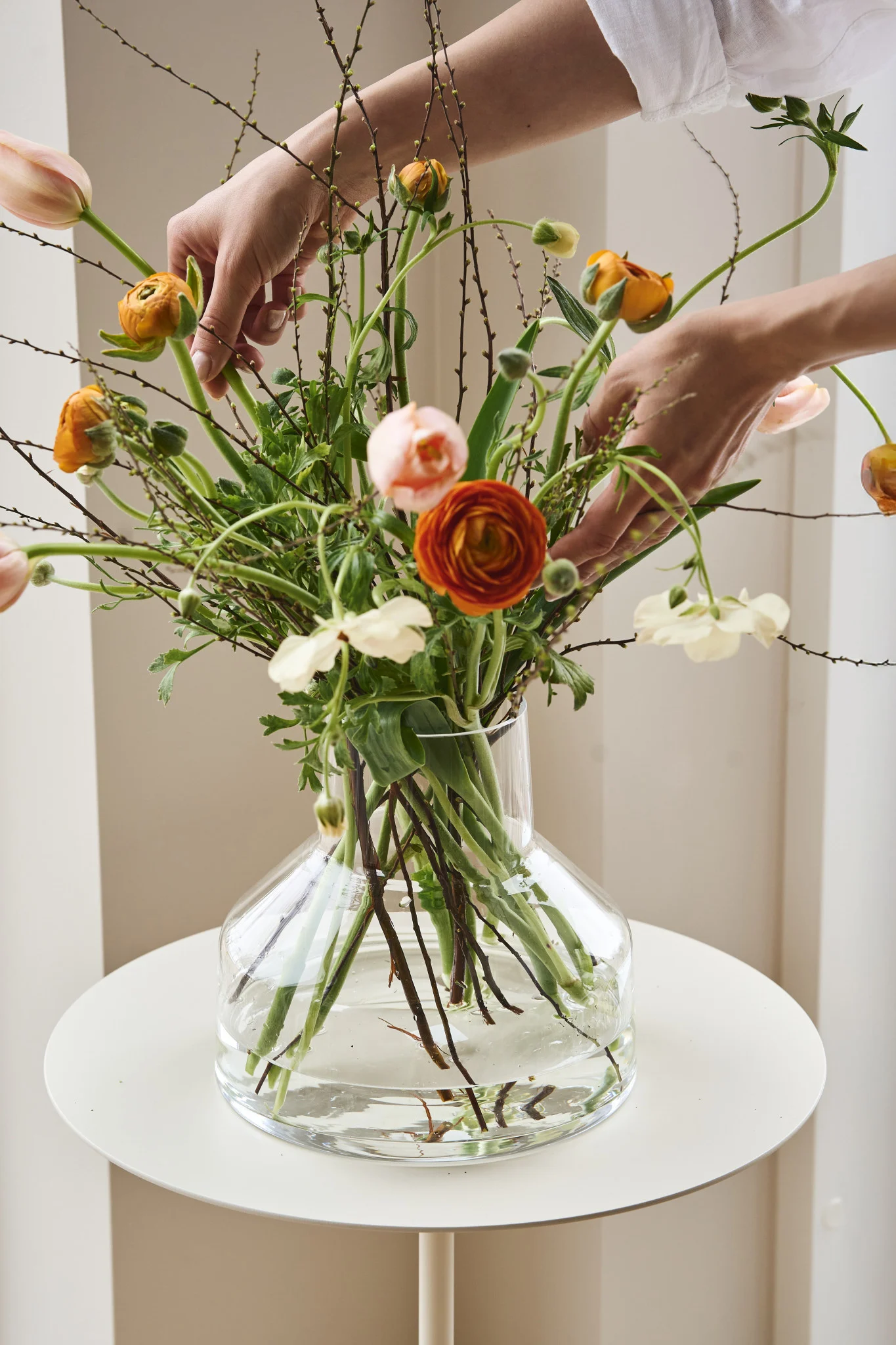 Here you see hands arranging flowers in a clear funnel shaped vases that is part of the Solare collection from Iittala. 