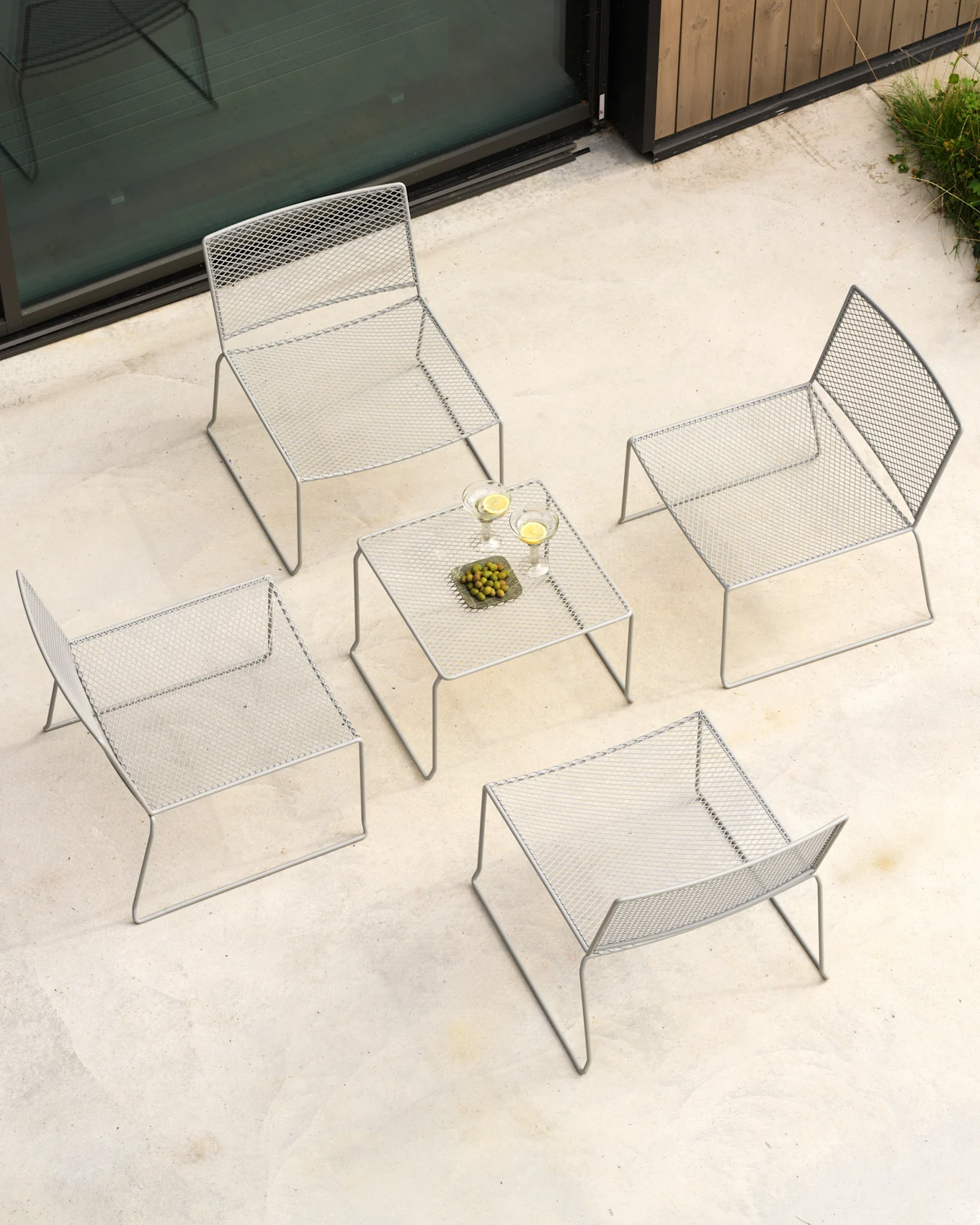 An aerial view of an outdoor patio set with four gray metal mesh chairs and a matching coffee table holding drinks and olives.