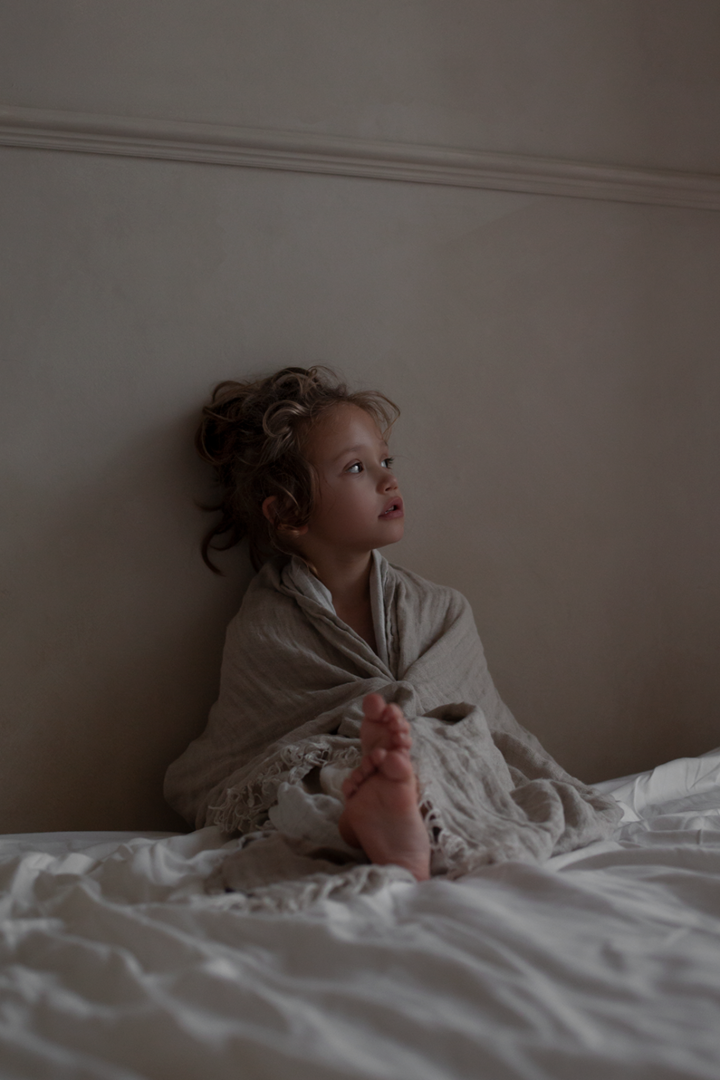 A boy sits on a bed wrapped in the Hannelin linen throw in beige from Himla