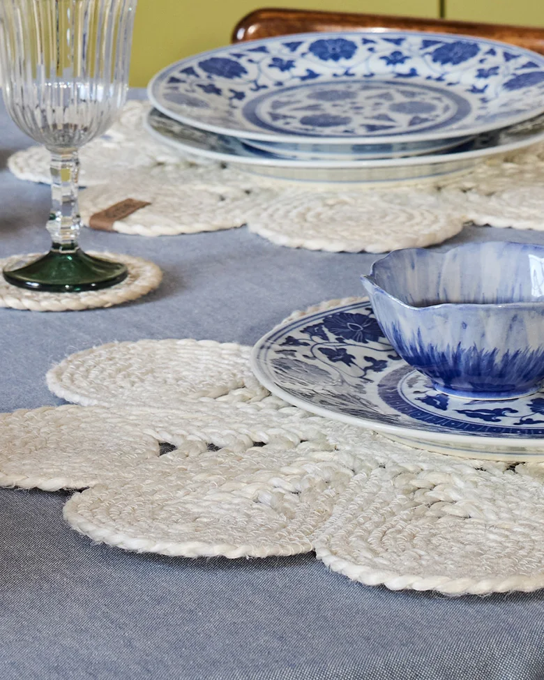 Table setting with blue and white dishes, white braided floral placemats, and a ribbed glass.