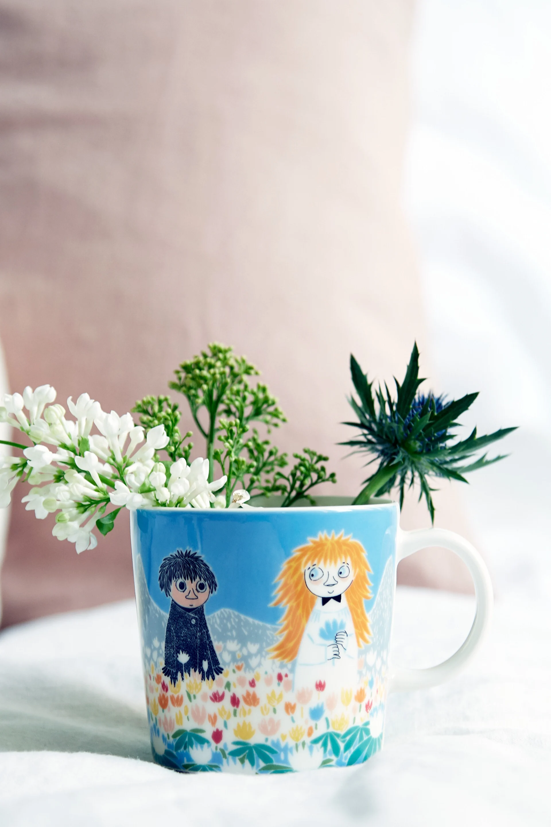 The Moomin cup ‘Friendship’ stands on a table with flowers inside.