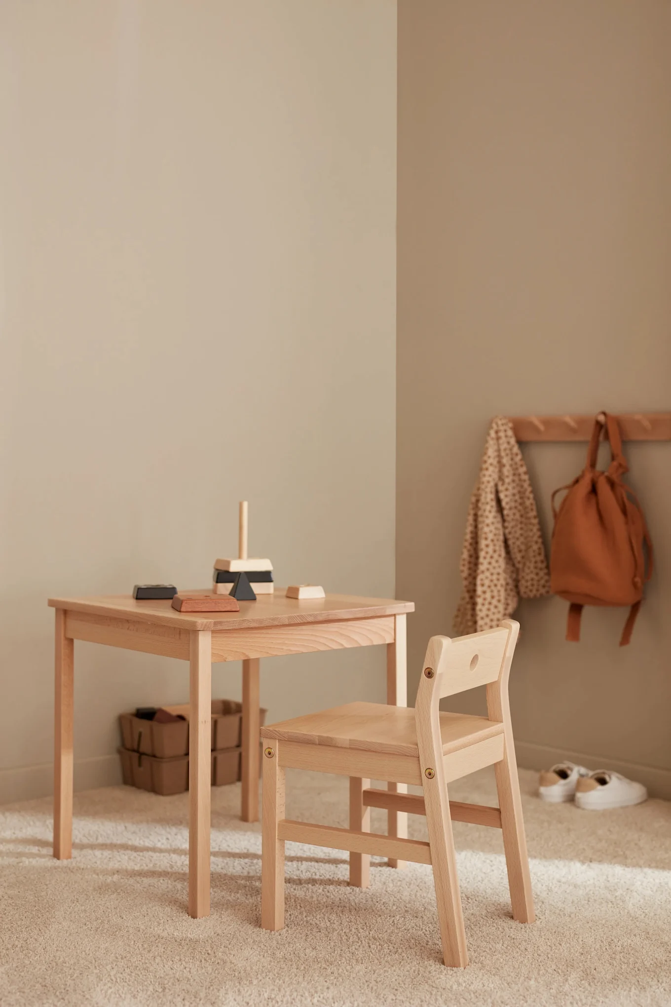 The Saga table and chairs in wood stand in a neutral coloured children's bedroom. 