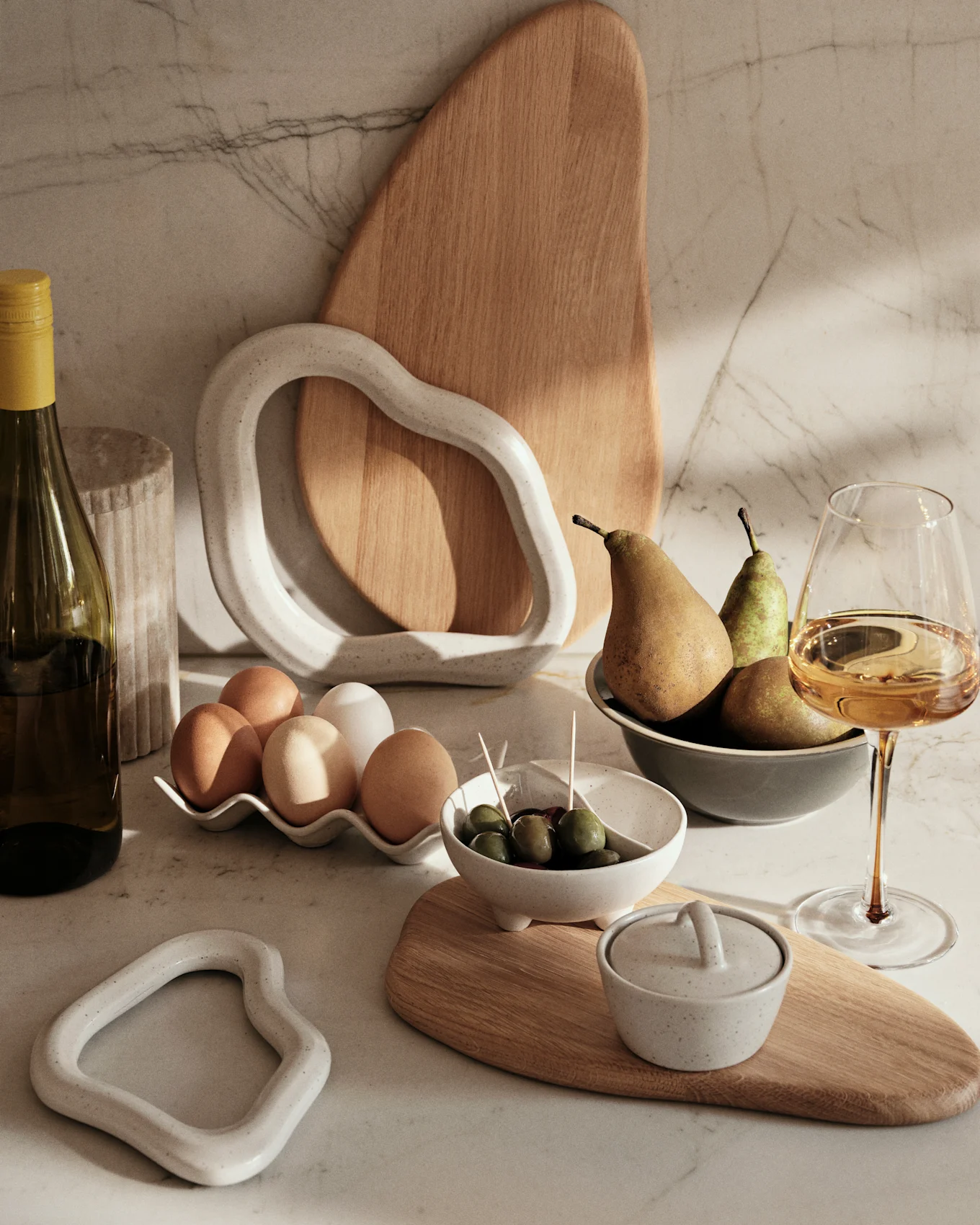Marble counter with a wine bottle, eggs, olives, pears, and decorative ceramic & wood items.