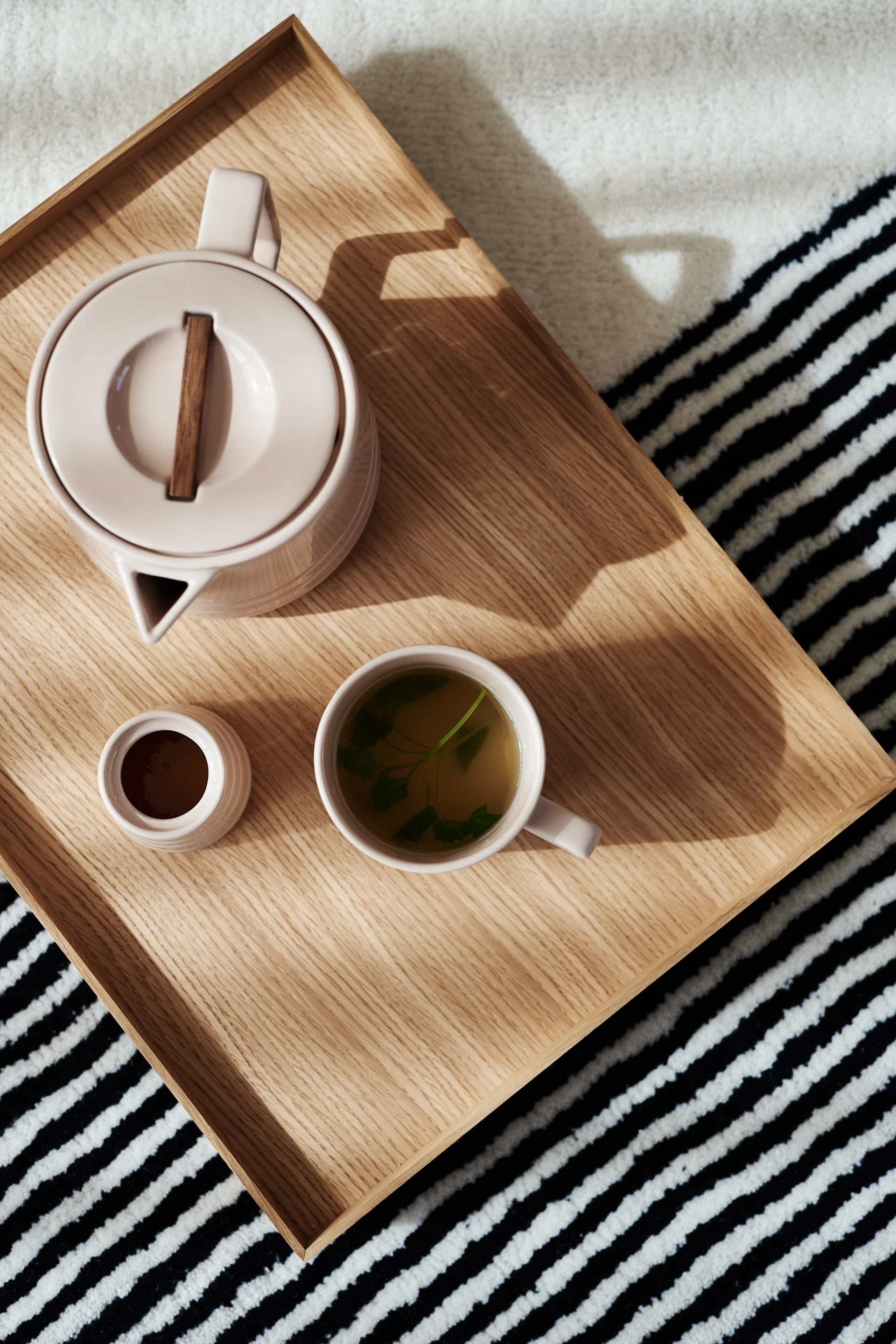 The NJRD Lines teapot, mug and sugar pot from above on a wooden tray with the Lines rug underneath.