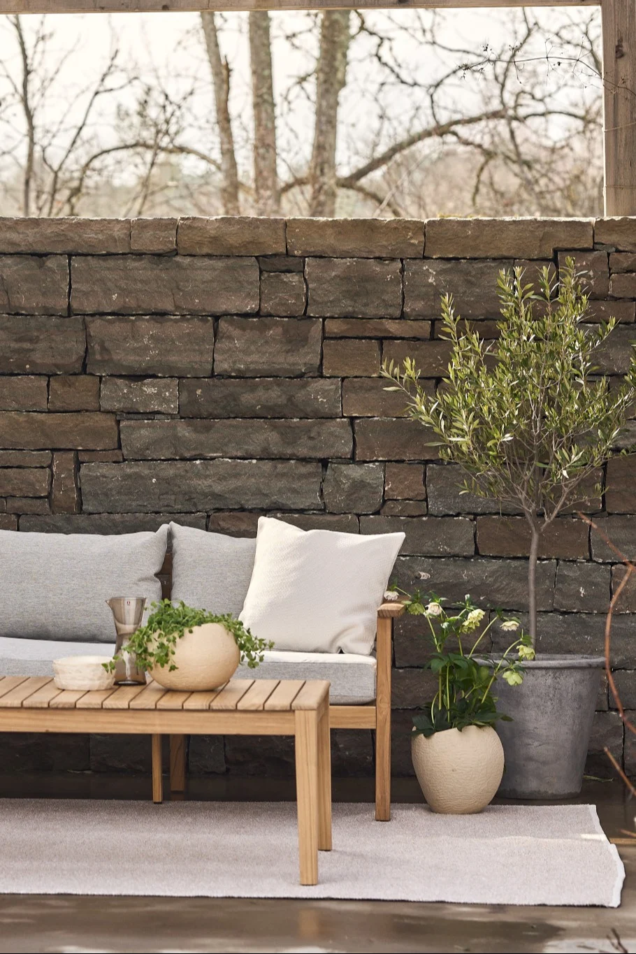 A cosy terrace with a carpet, a sofa and a side table, next to numerous plants.