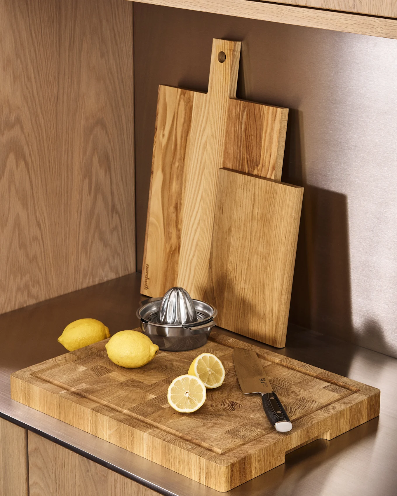 Kitchen counter with three wooden cutting boards, a metal lemon juicer, whole and halved lemons, and a knife.