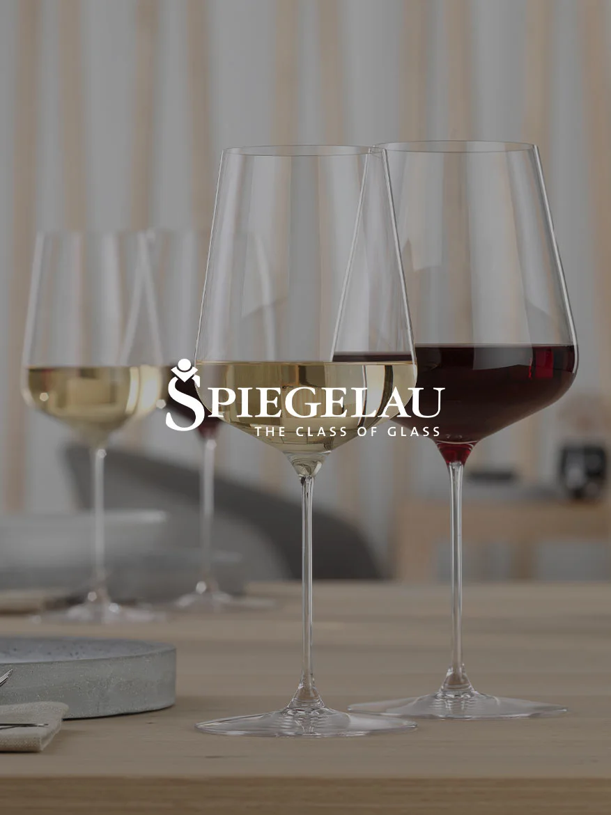 Two Spiegelau wine glasses on a wooden table, one filled with white wine and one with red wine.