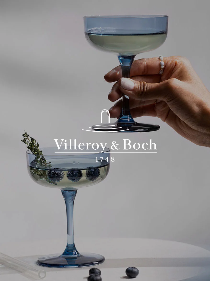 Hand holds blue coupe glass; another glass below with blueberries, thyme, and Villeroy & Boch logo and '1748'.