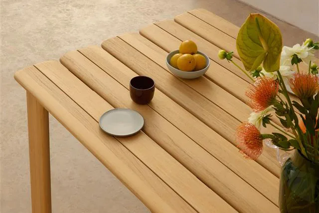 Light wooden slatted table with a bowl of lemons, dark mug, small plate, and a vase of orange and white flowers.