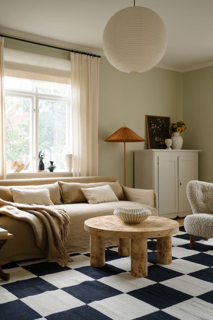 Image showing the Rice paper lampshade from HAY, hanging in a living room with a beige sofa, black and white checked carpet and a rustic wooden coffee table.