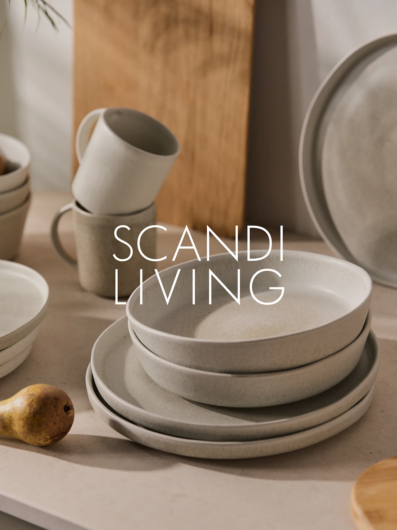 Stack of light speckled ceramic plates, bowls, and mugs with a pear. Text: SCANDI LIVING.