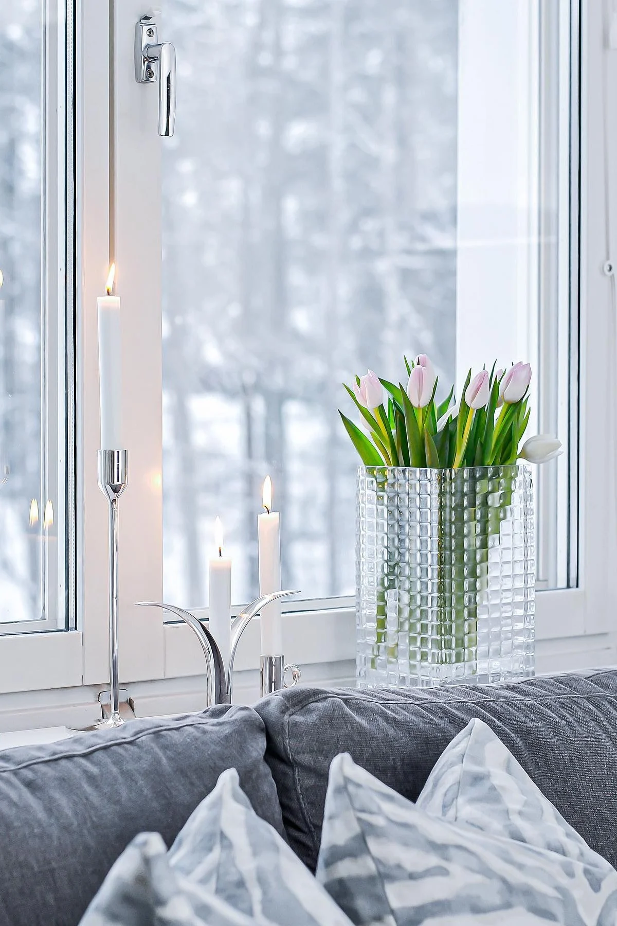 Decorate your windowsill with candles or pretty flowers, especially in the darker months. Here you can see fresh tulips in the City Hurricane vase by Louise Roe, next to various silver candlesticks with white candles in them on the windowsill by @josefinsinredning.