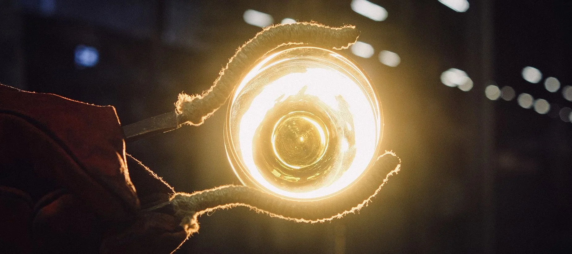 A pair of tongs hold up a glowing piece of glass art at the Iittala glass works in Finland.