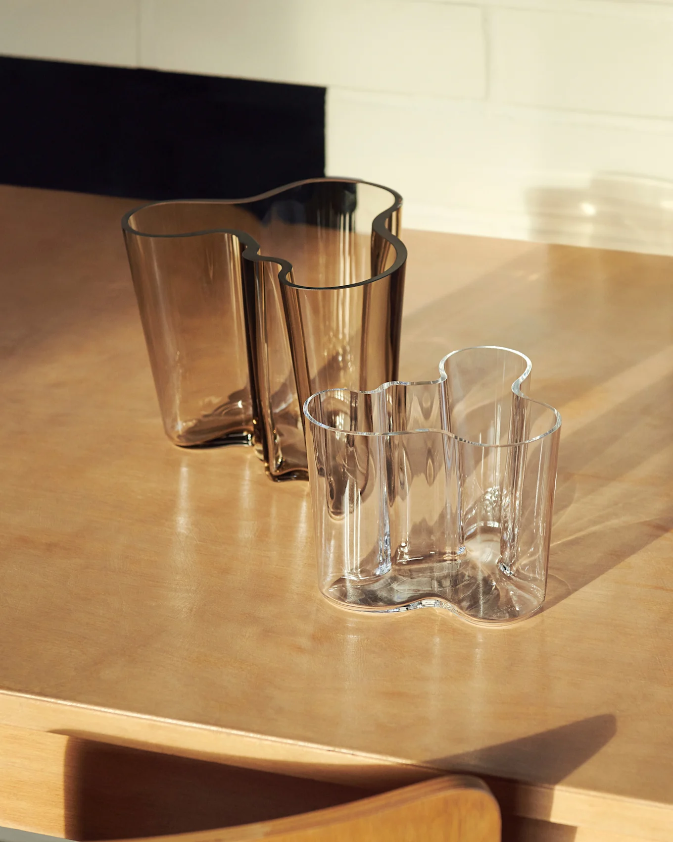 Two wavy glass vases, one large amber and one smaller clear, on a wooden surface.