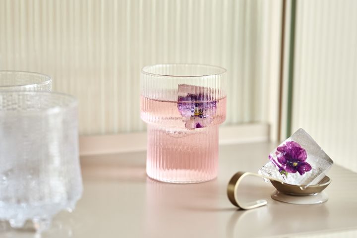 Ripple drinking glass from Ferm Living with a pink drink and purple flower frozen in an ice cube.