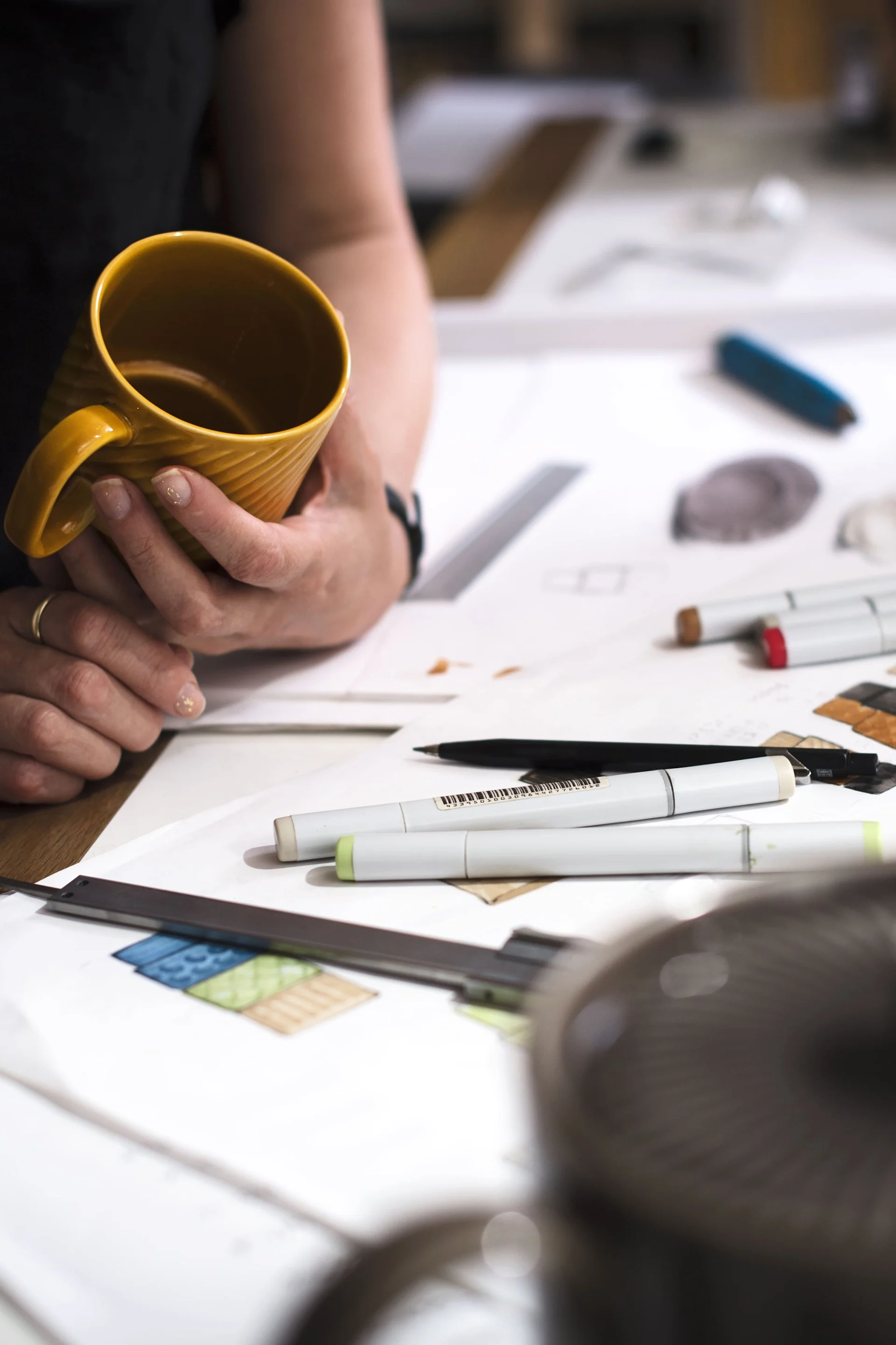 A table with paper and pens, next to it stands a person holding a yellow coffee mug from Sagaform's Coffee & more collection.