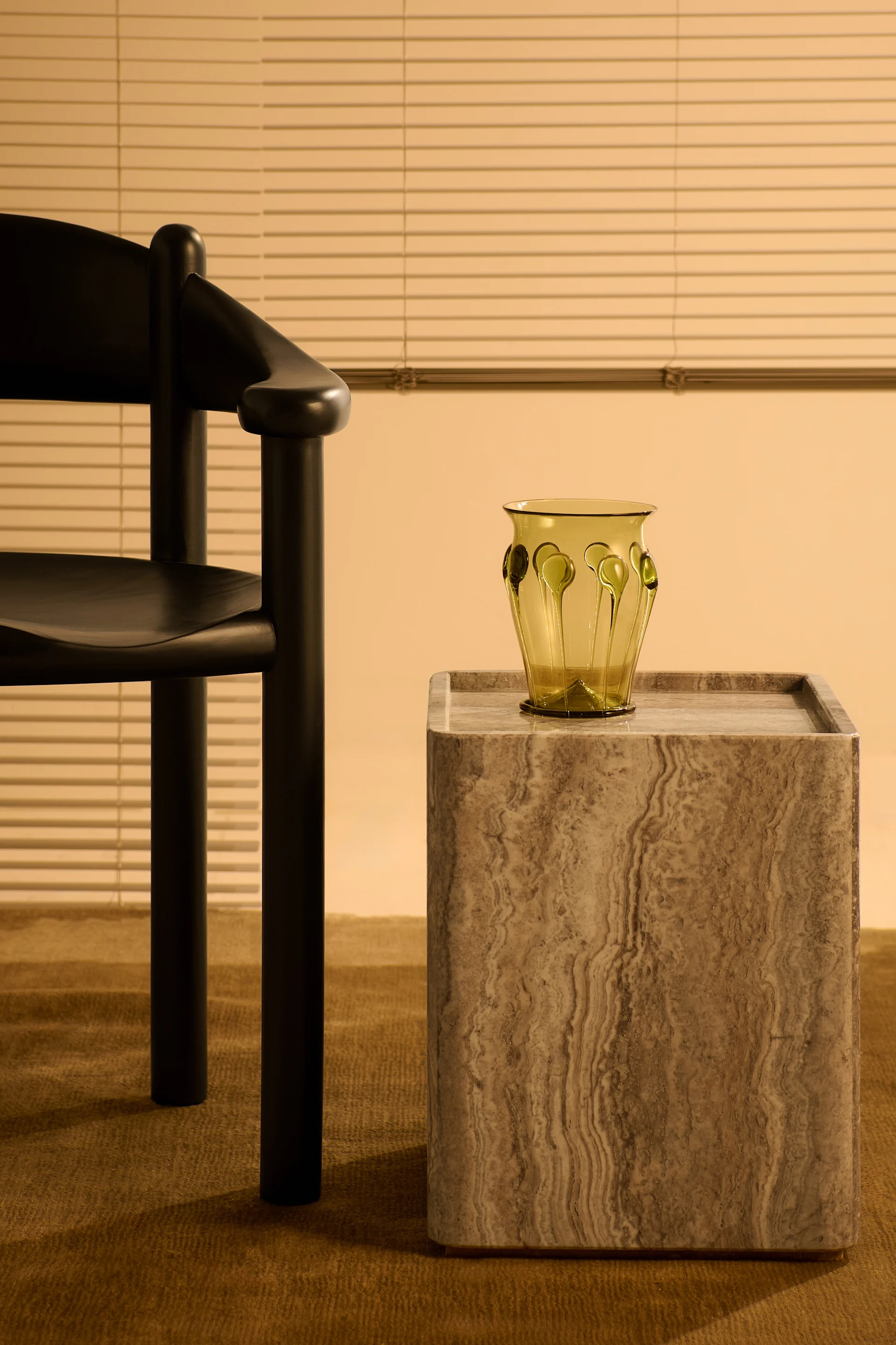 Stone, one of the interior design trends in autumn 2025, is here in the form of the Peitra side table from Gubi next to a chair with a vase on top.