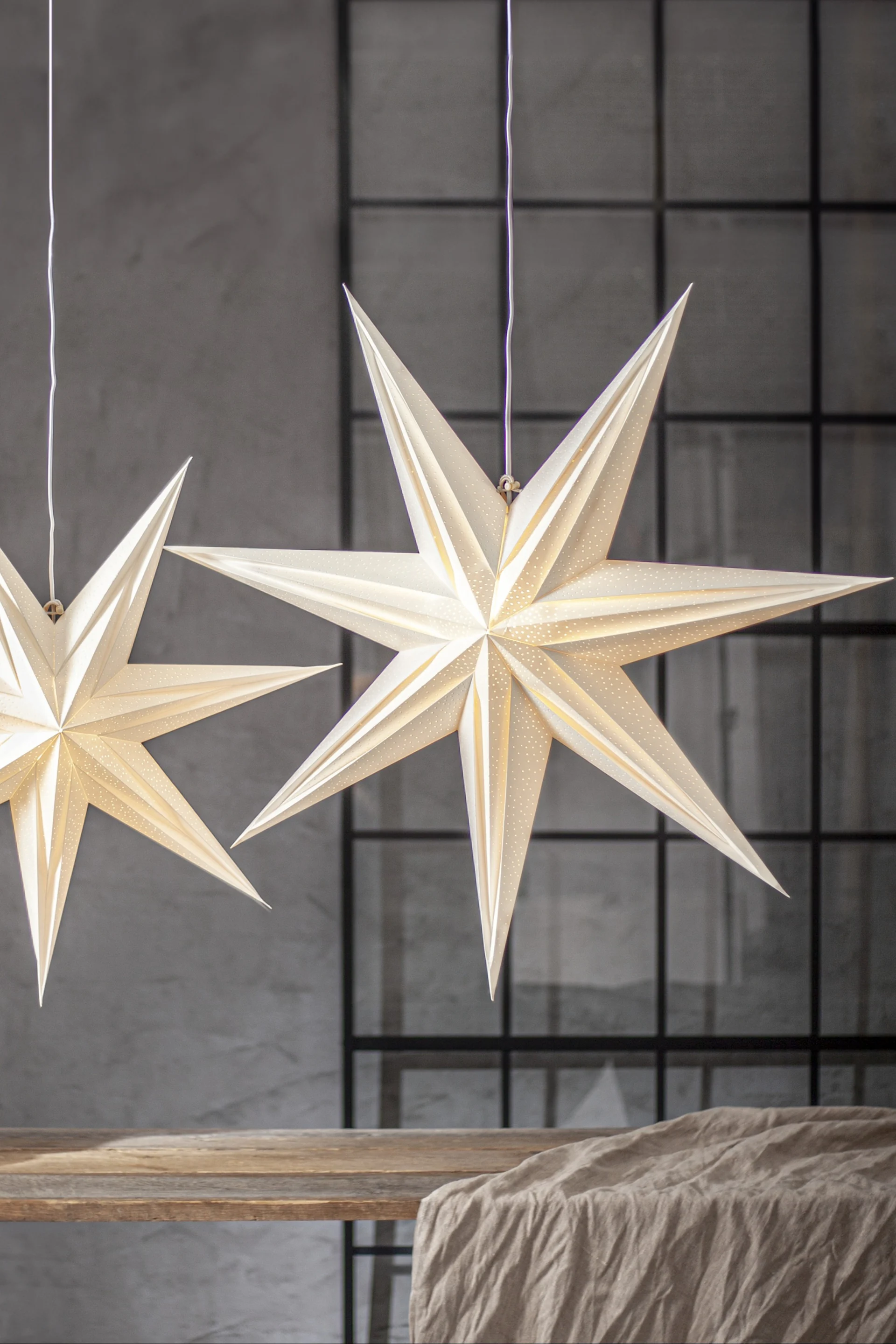 A seven point paper star lantern from Star Trading hangs together with a smaller version over a wooden table. 