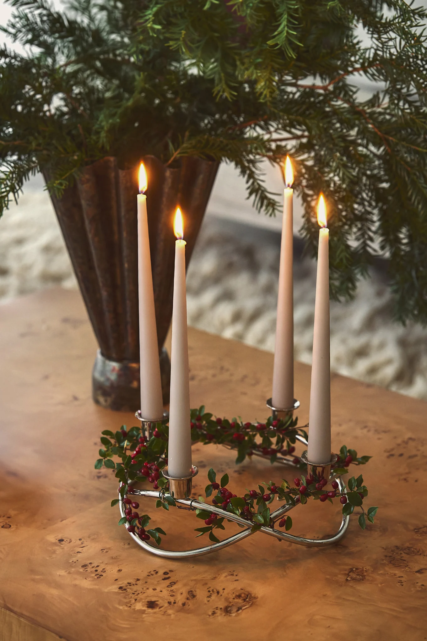 An Advent candle holder from Georg Jensen stands on a wooden coffee table alongside a vase of fir branches.