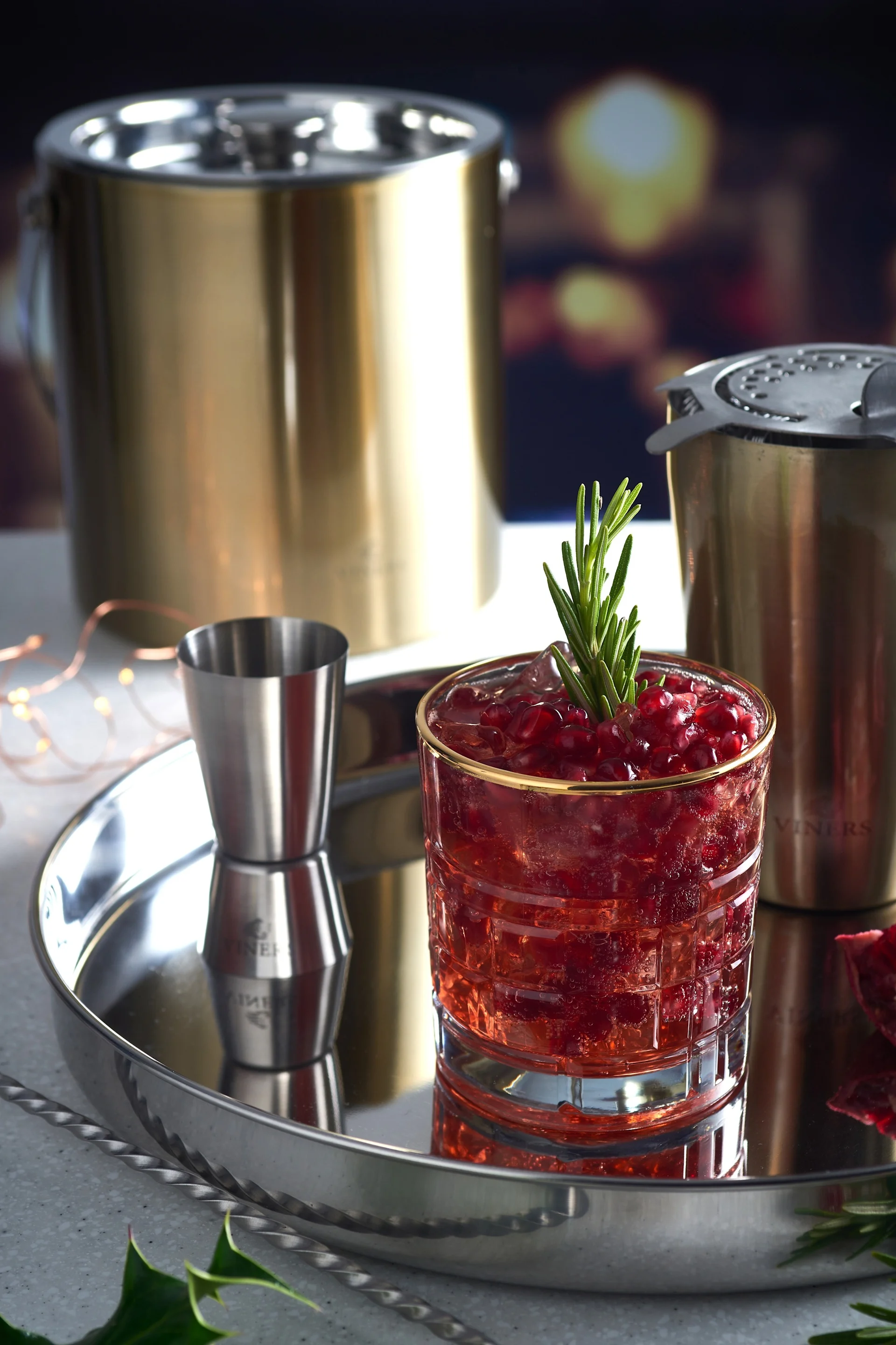 A mocktail sits on a silver tray, next to cocktail utensils like a shaker and the golden ice bucket from Viners.