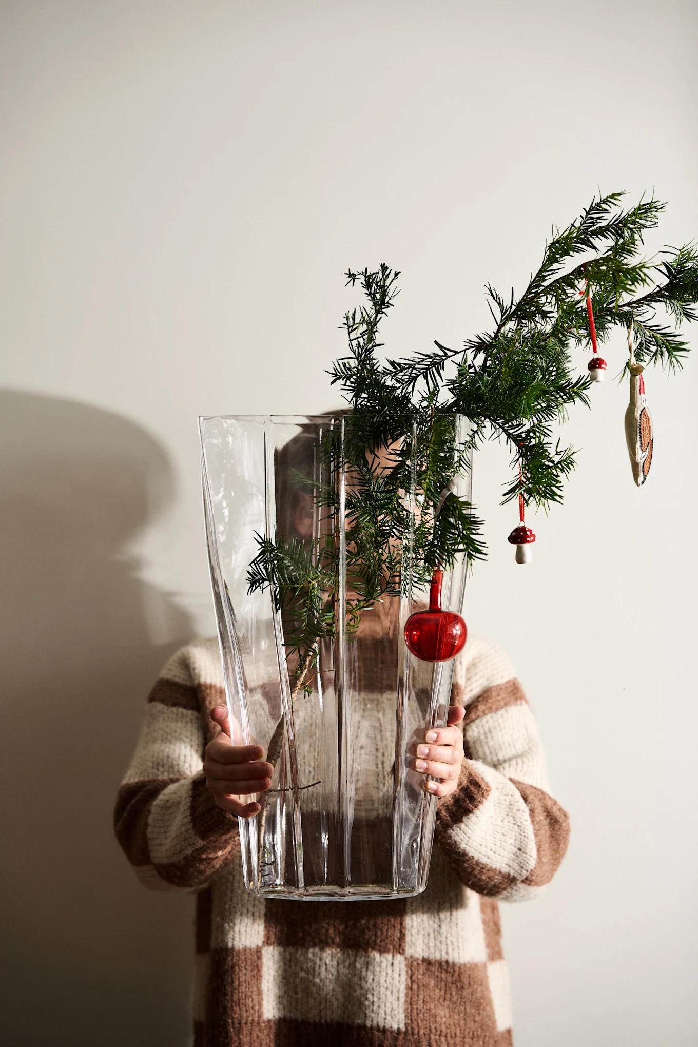 Hands hold out the Reed vase from Orrefors with vintage Christmas decorations hanging from a pine branch.