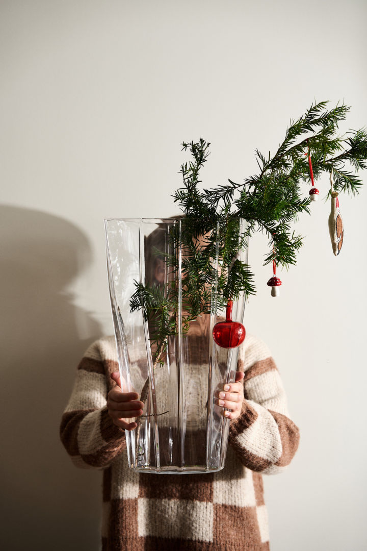 Hands hold out the Reed vase from Orrefors with vintage Christmas decorations hanging from a pine branch. 