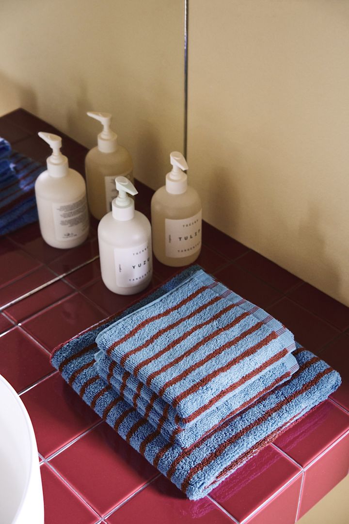 The striped towels from the Drift collection by Scandi Living are absolutely on trend for autumn 2025. Here they are carefully folded on a red tiled shelf.