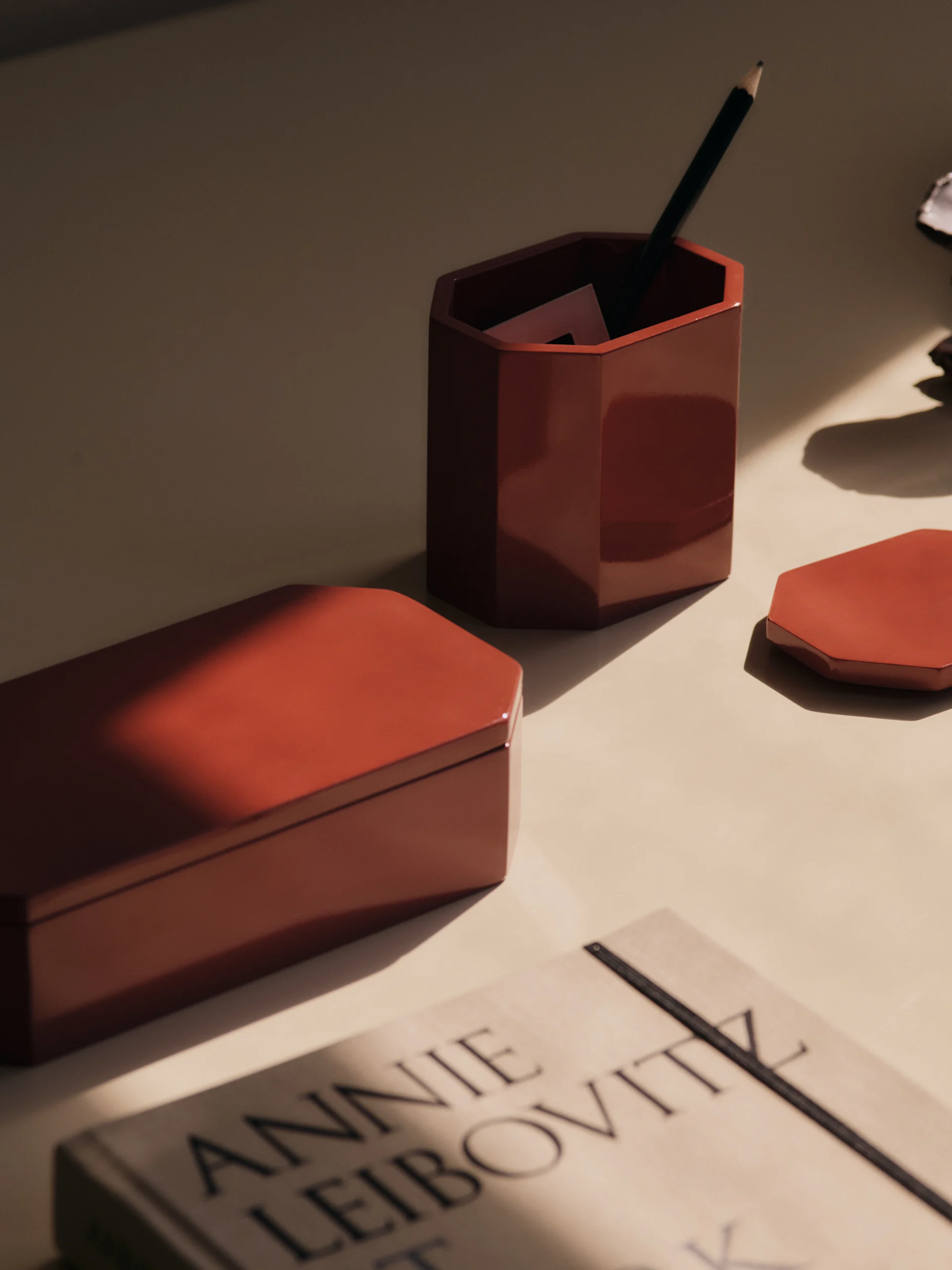 A desk with red hexagonal storage items, a pencil holder, and a book, bathed in sunlight.