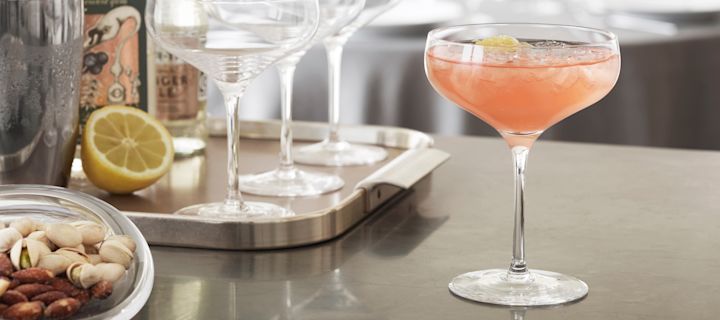 A mocktail with grapefruit juice in a Holmegaard Cabernet cocktail glass sits on a kitchen counter with cocktail utensils in the background.