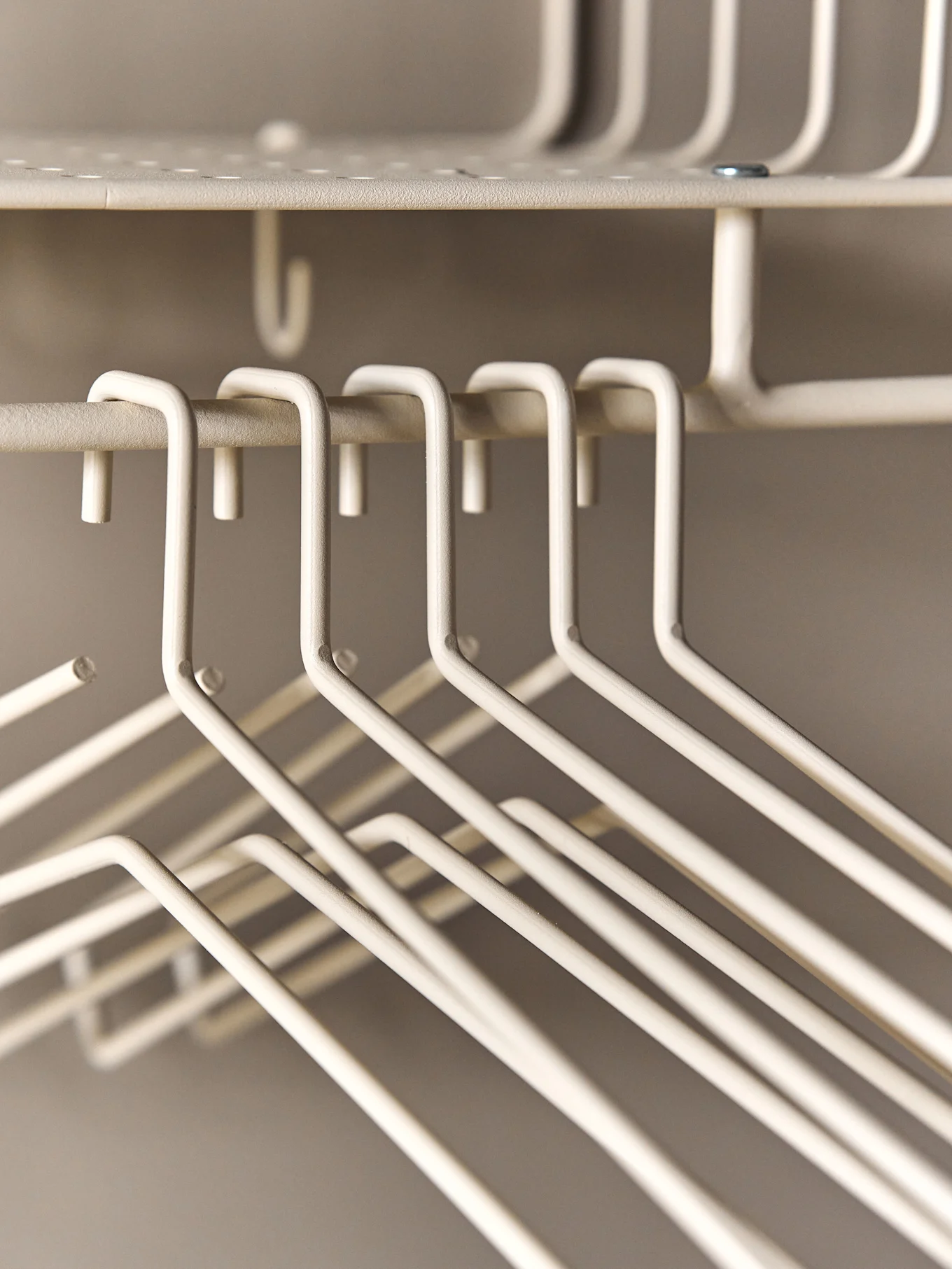 A close-up of several empty cream-colored wire clothes hangers hanging on a wire rack.