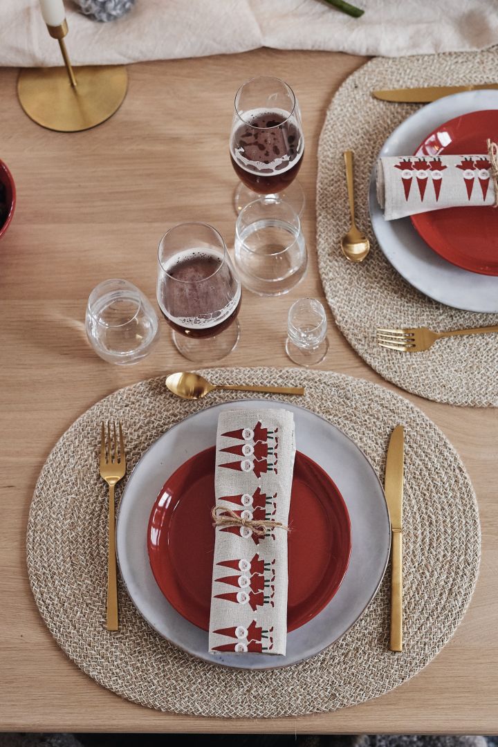 A simple Christmas table decoration where the place setting consists of a blue-gray plate, a red plate and gold cutlery.