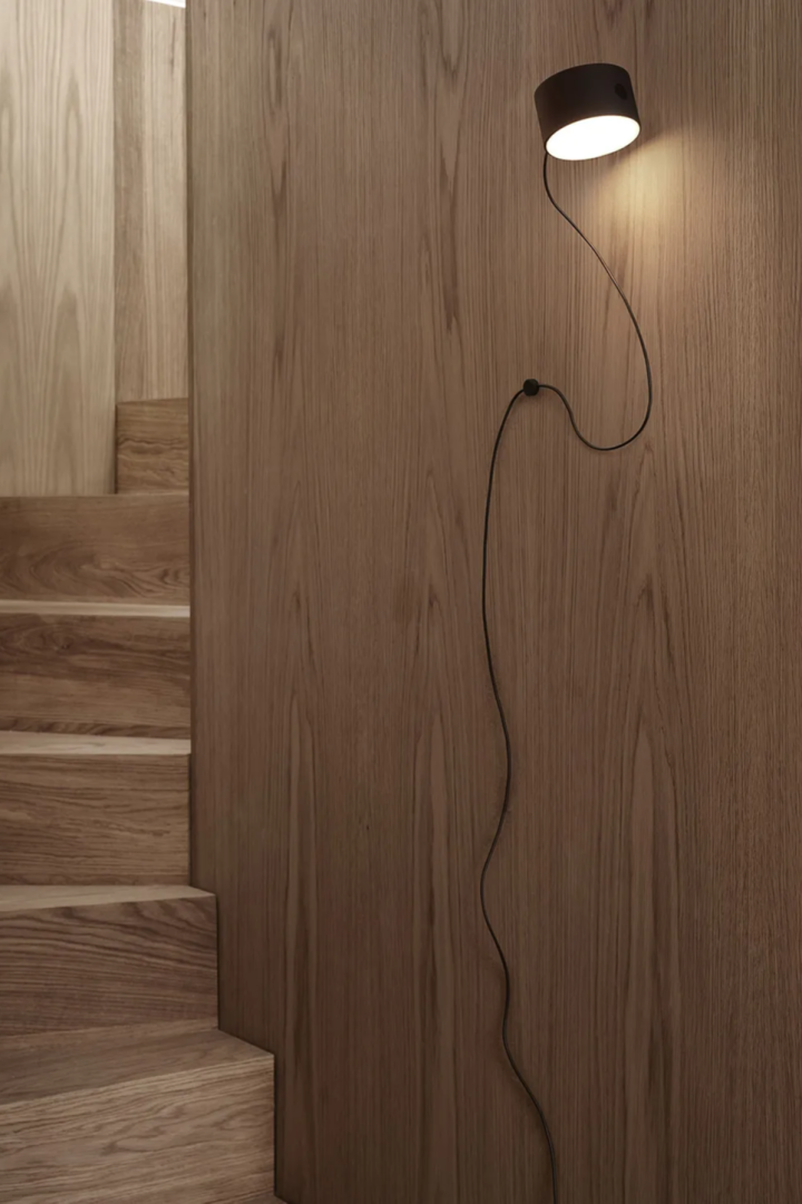 The Post wall lamp from Muuto hangs in an entirely wooden stairway.
