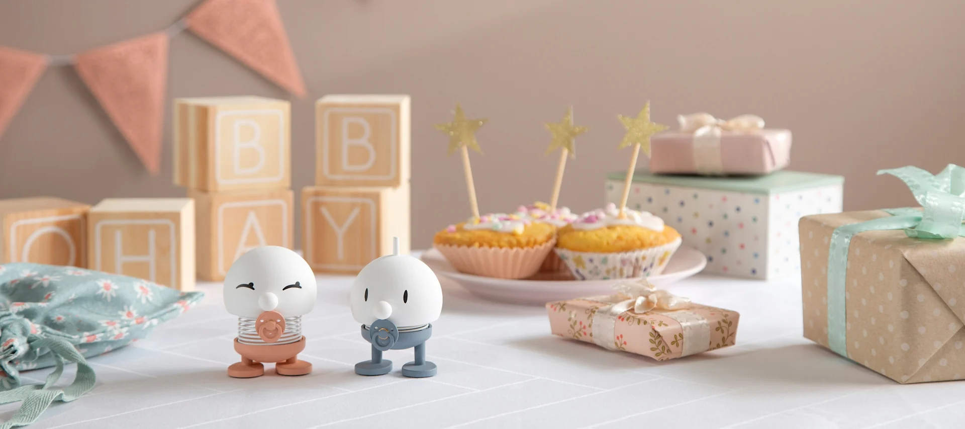 The Hoptimist Baby Bimble is available in pink and blue and stands on a table decorated with presents, garlands and cupcakes.