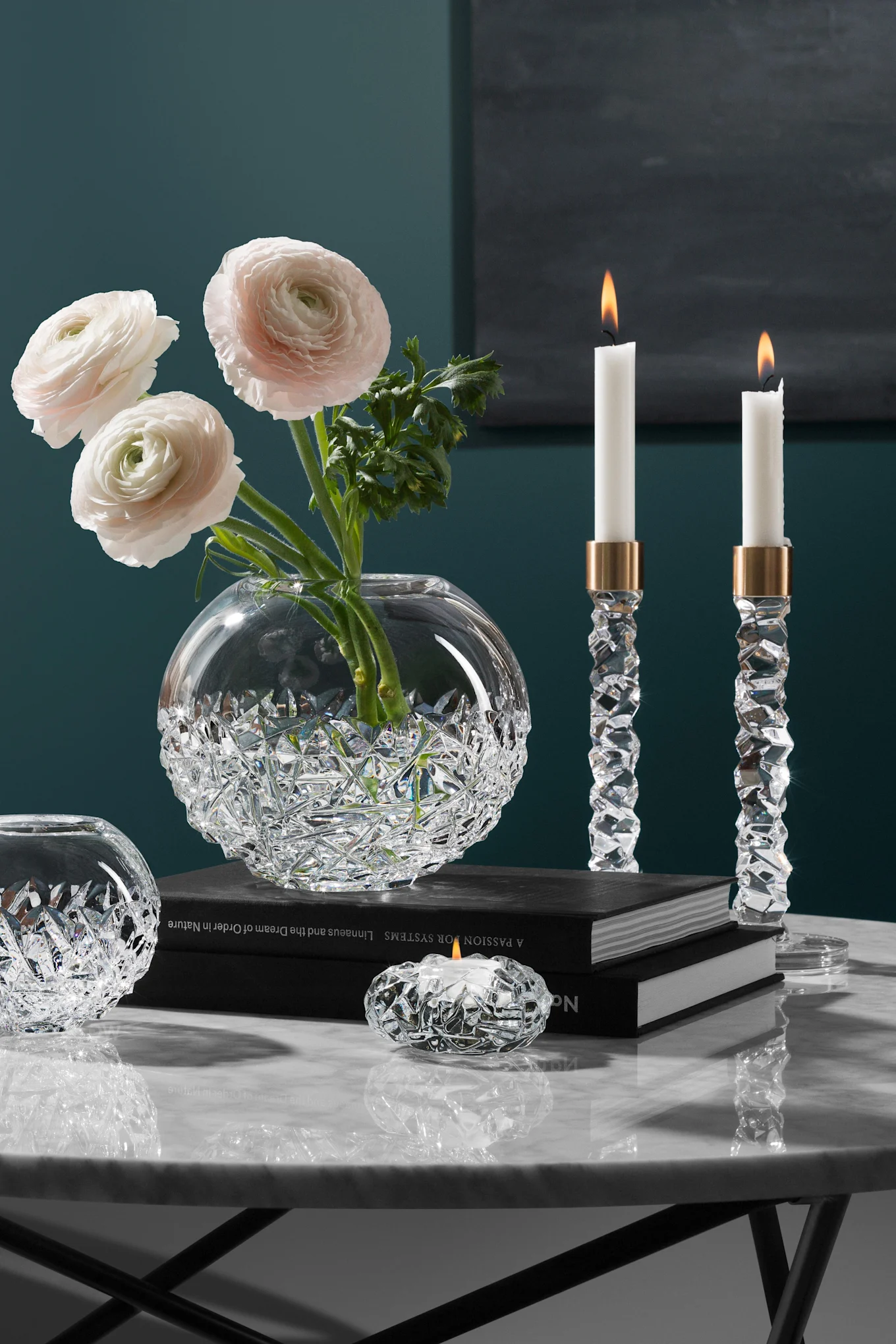 Elegant crystal vase with pink ranunculus, two lit crystal candlesticks, and a tea light holder on a marble table.