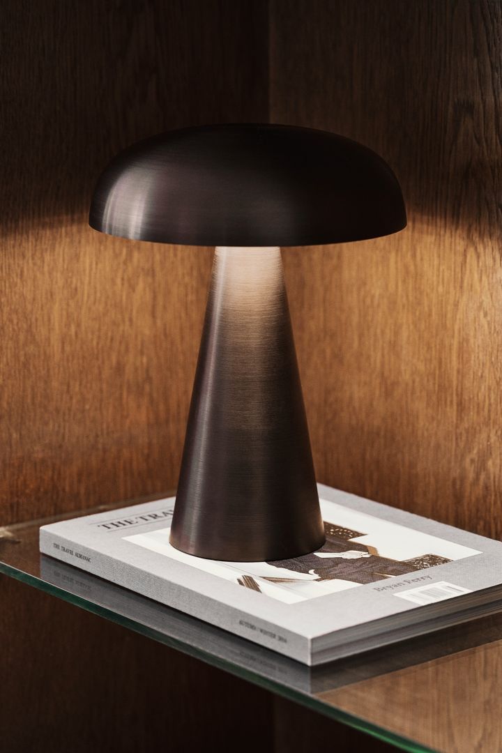 The &Tradition portable Como table lamp in dark brown sits wooden bookshelf - all components that reflect the autumn interior design trends 2021.