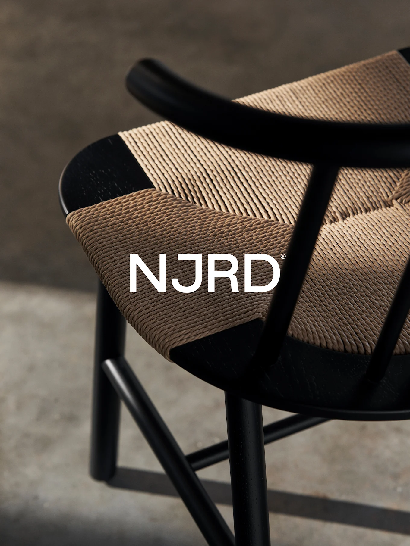 Close-up of a black chair with a woven light brown seat, featuring the white 'NJRD' logo.