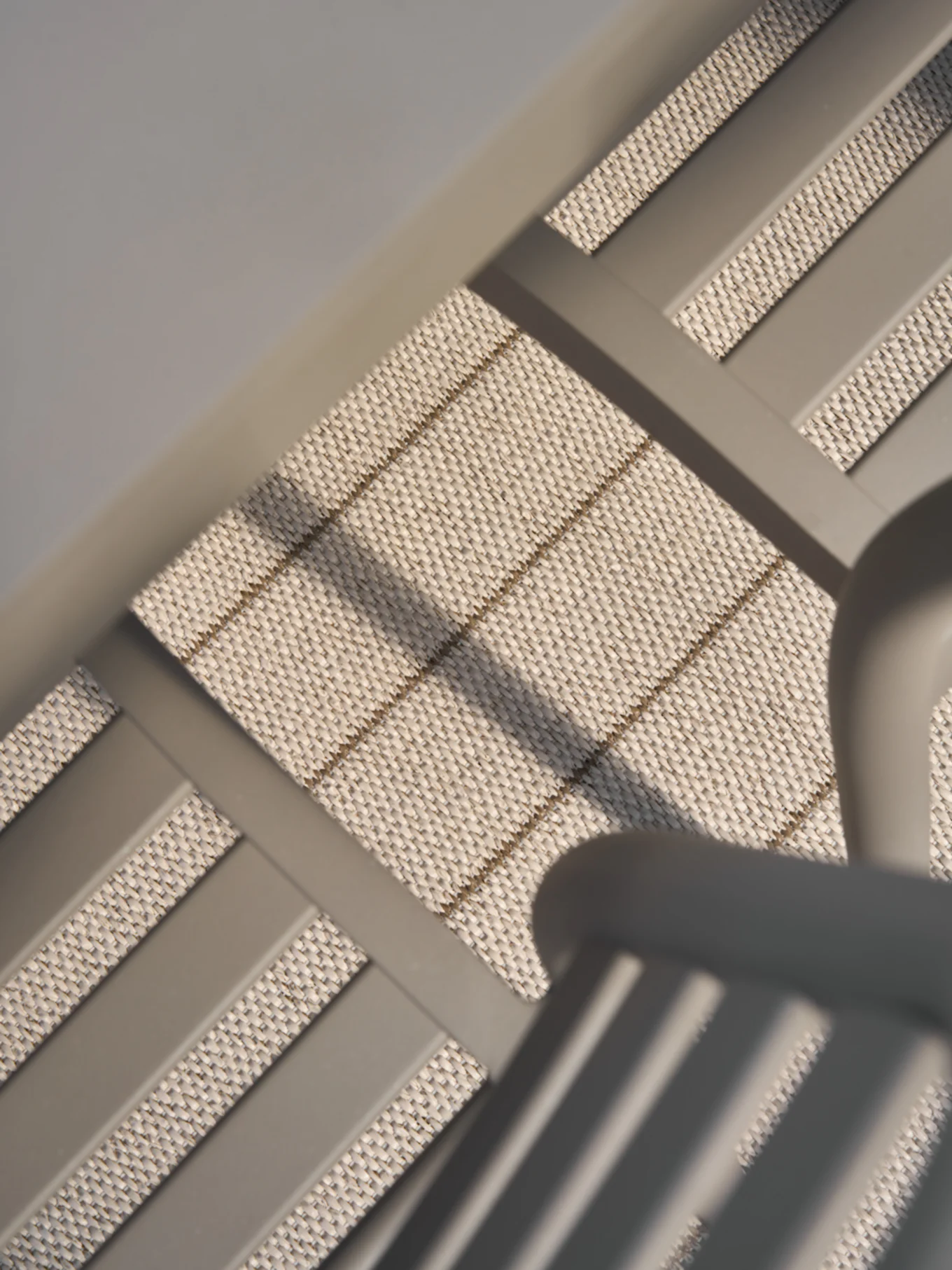 Close-up, angled view of light beige woven material with subtle horizontal and diagonal brown stripes, framed by smooth gray bars.